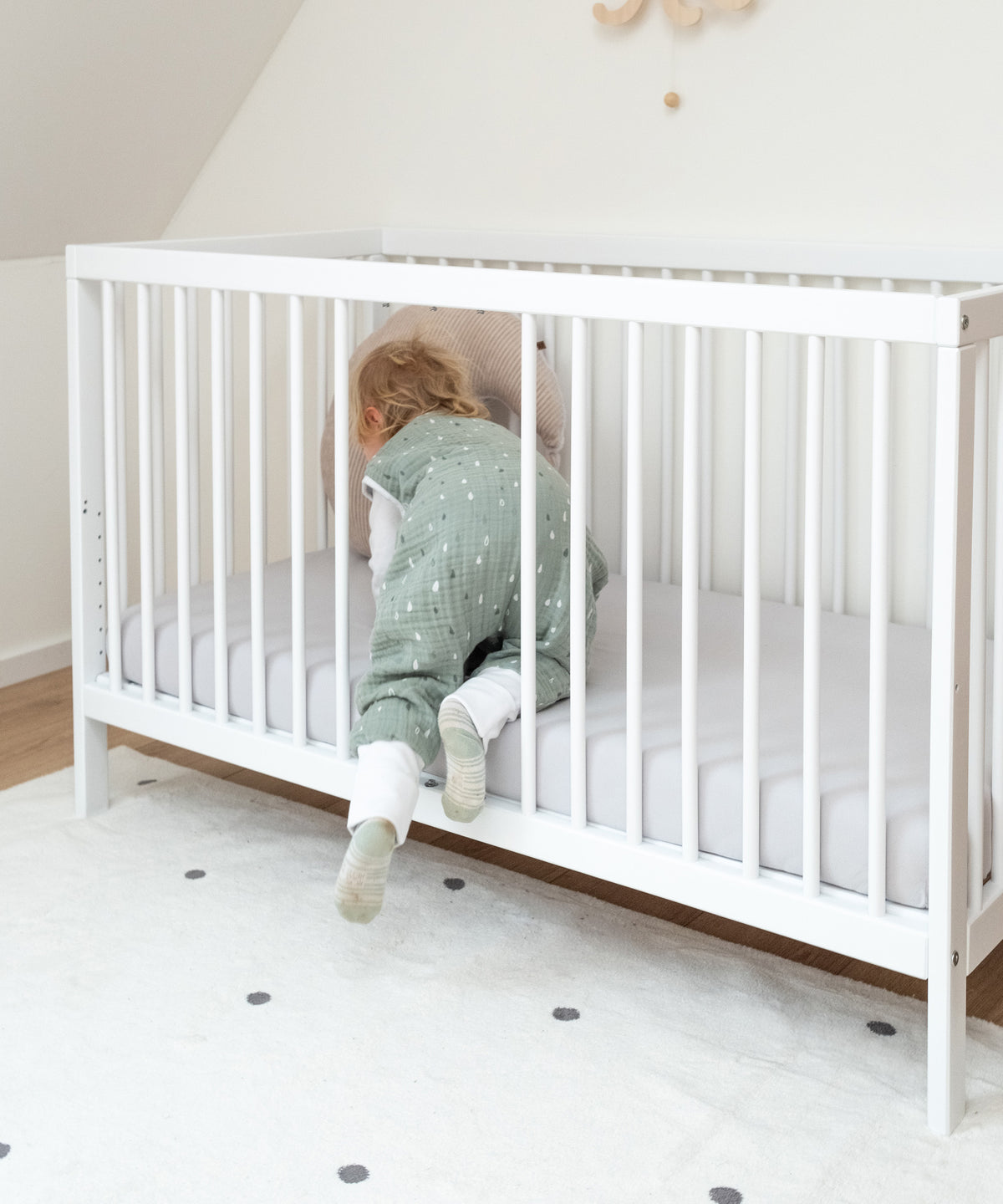 Kind krabbelt durch Öffnung in Babybett weiß.