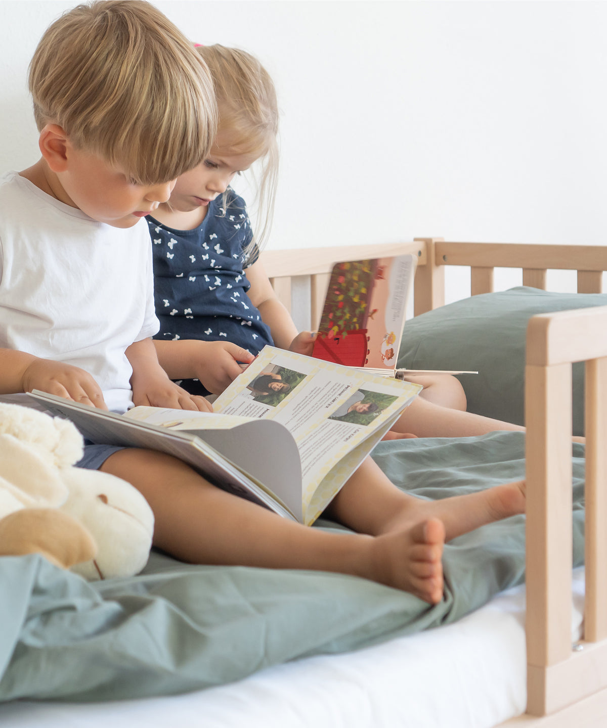 Zwei Kinder sitzen auf Kinderbett und schauen Bilderbücher an.