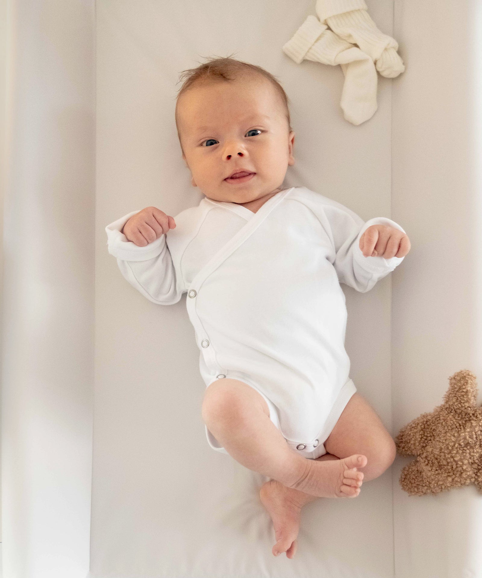 Baby liegt auf abwaschbarer Wickelauflage in Beige.