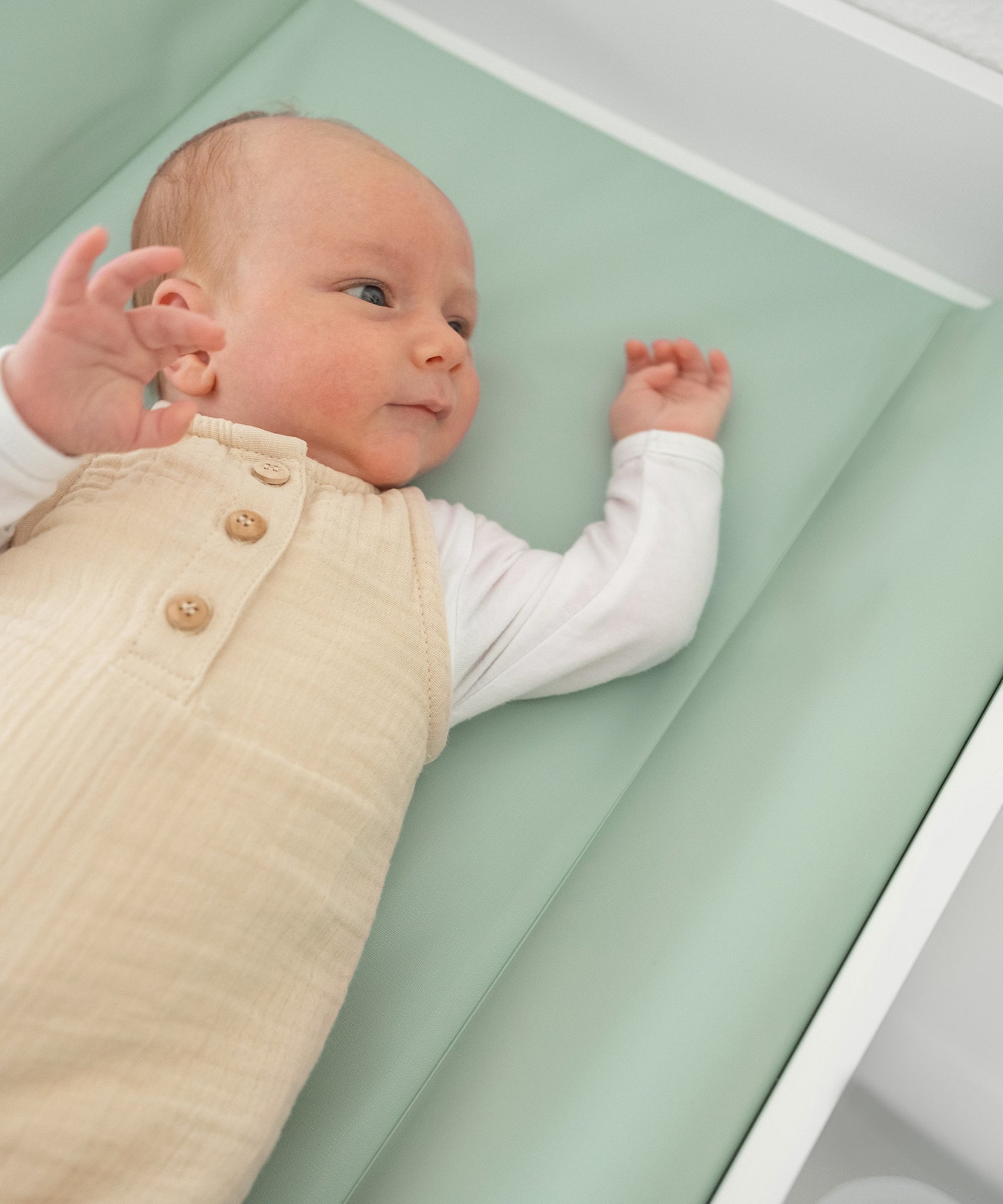 Baby liegt auf Wickelauflage abwaschbar 50x70 in Jade.