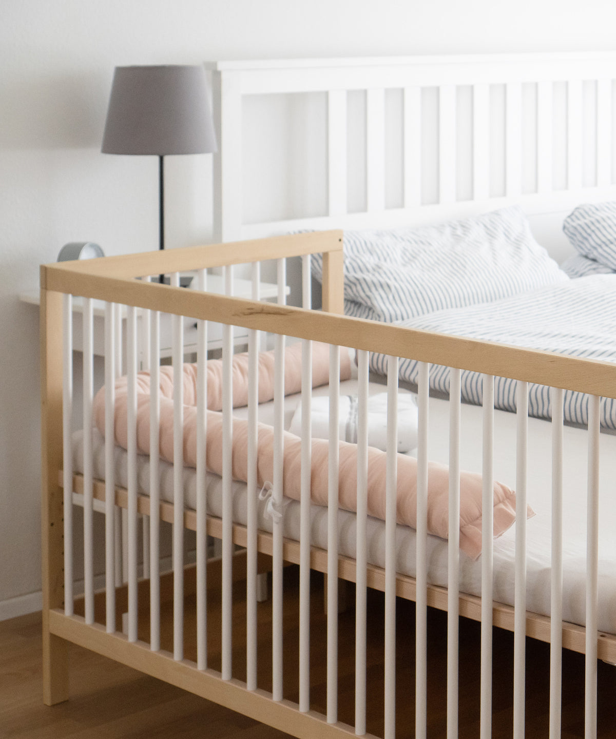 Babybett mit offener Seite steht als Beistellbett direkt neben dem Elternbett.
