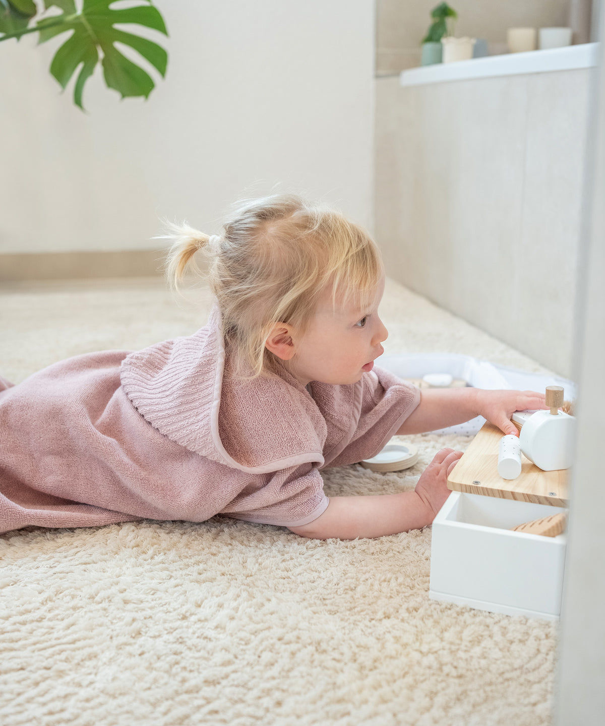 Mädchen in Badeponcho rosé spielt auf Badezimmer-Teppich.