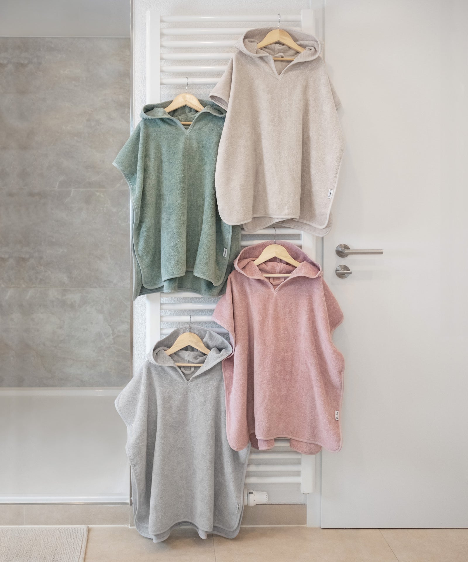 Tolle Farben*Für jeden Geschmack etwas dabei: Unser Badeponcho ist in den vier frischen Farben Jade, Rosé, Hellgrau und Beige erhältlich.|Badeponchos in vier Farben hängen auf Kleiderbügeln in Badezimmer.