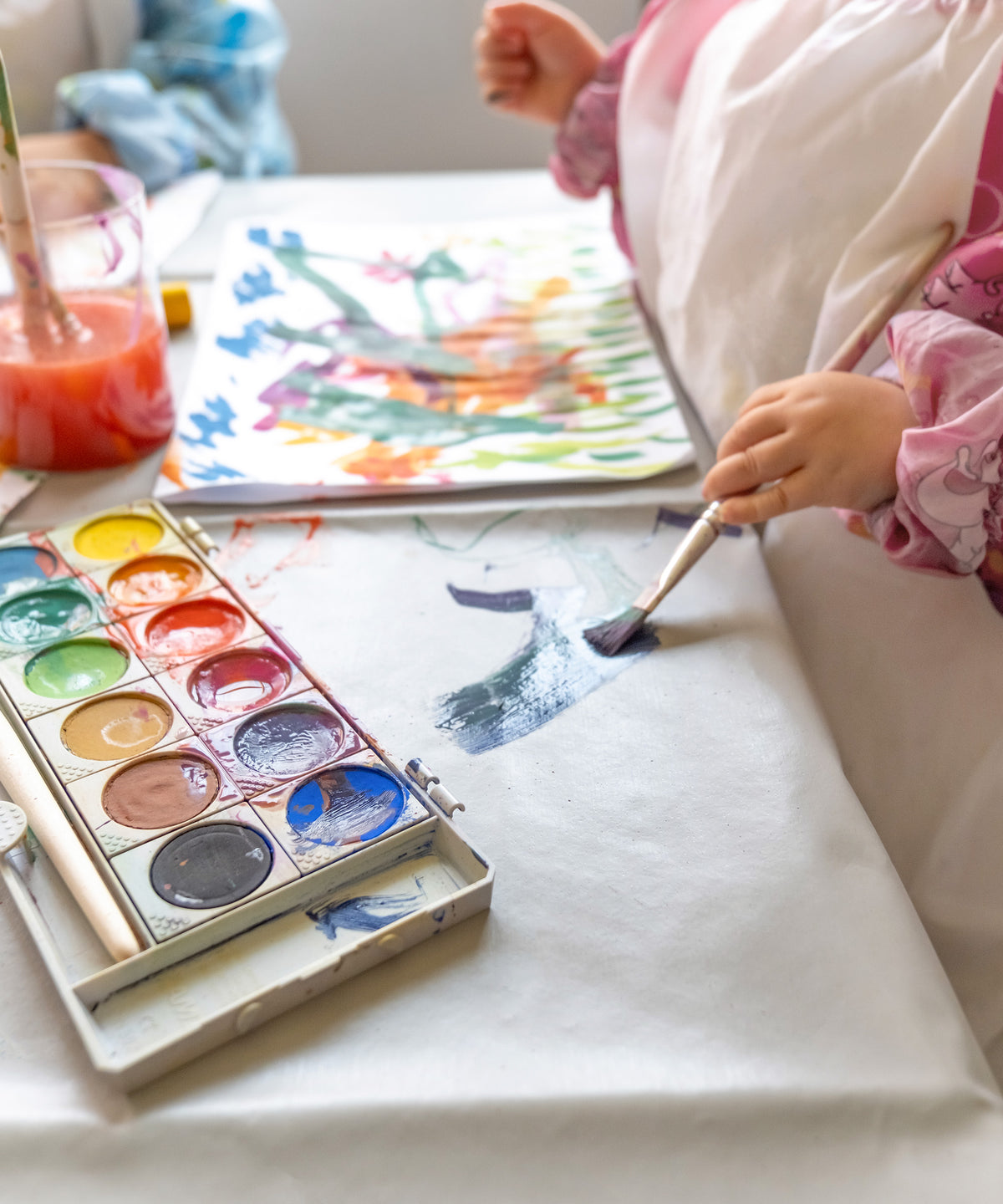 Kinder malen mit Wassermalfarben auf der Mal- und Bastelunterlage.