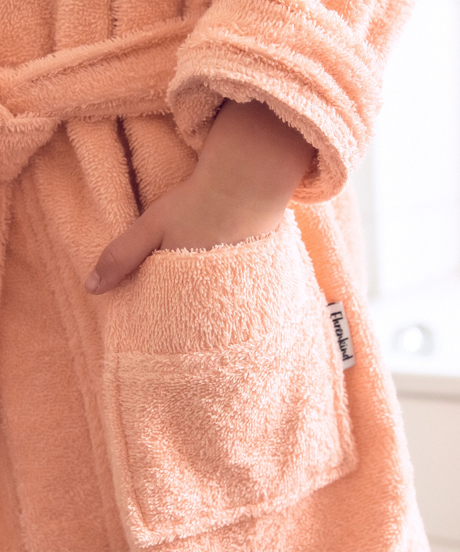 Einfach gemütlich*Dank aufgesetzter Taschen und wärmender Kapuze kann sich dein Kind so richtig in den gemütlichen Bademantel einkuscheln.|Kind steckt die Hand in die Tasche des Bademantels.