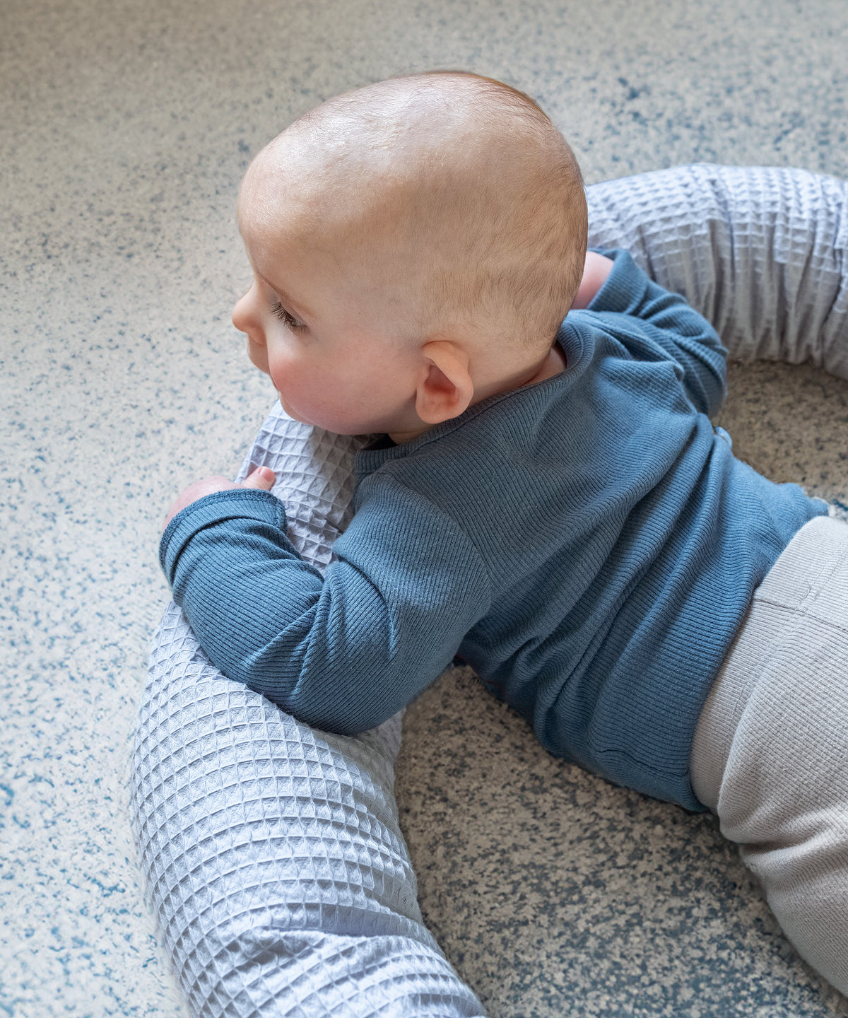 Baby liegt mit Bettschlange auf Teppichboden.