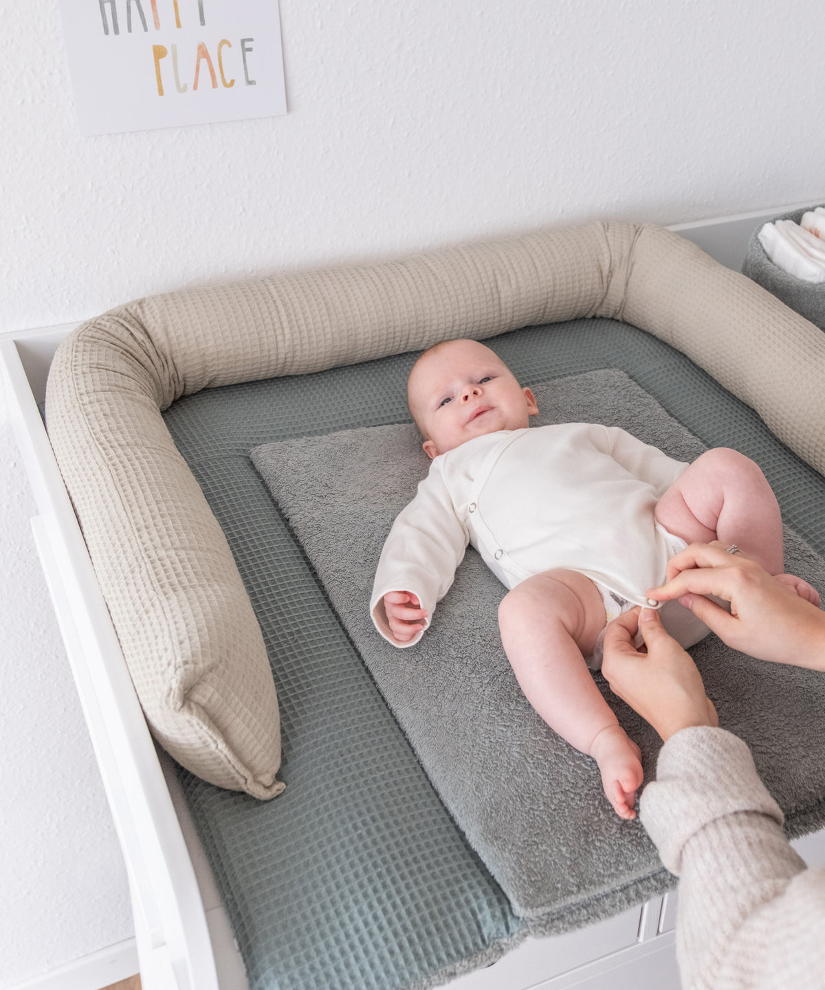 Baby liegt auf dem Wickeltisch, am Rand rundherum liegt die Bettschlange in beige.