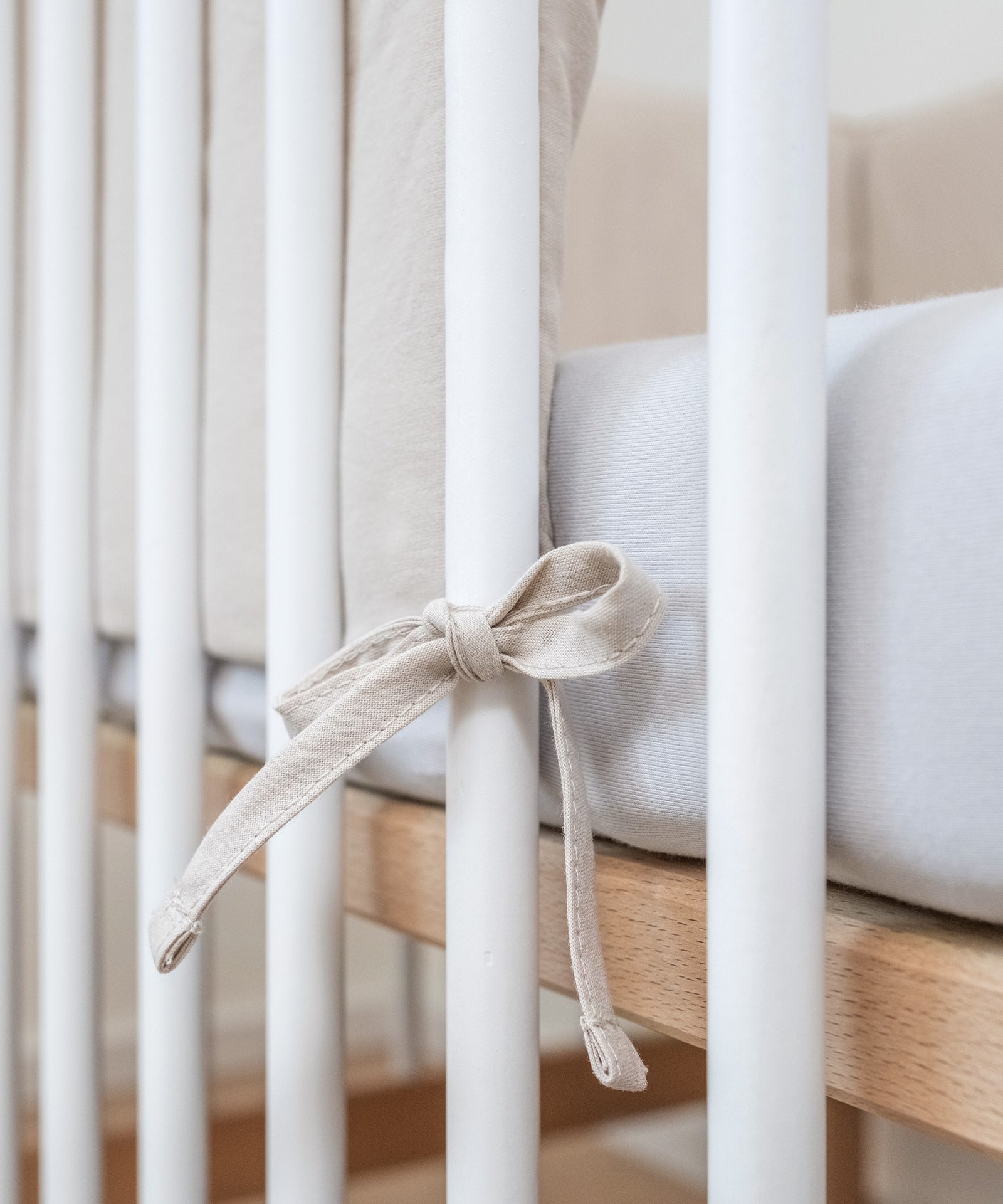 So praktisch*Mittels Befestigungsschnüren kann die Bettumrandung gleichmäßig an den Streben befestigt werden.|Nahaufnahme Befestigungsschnüre an Gitterstab.