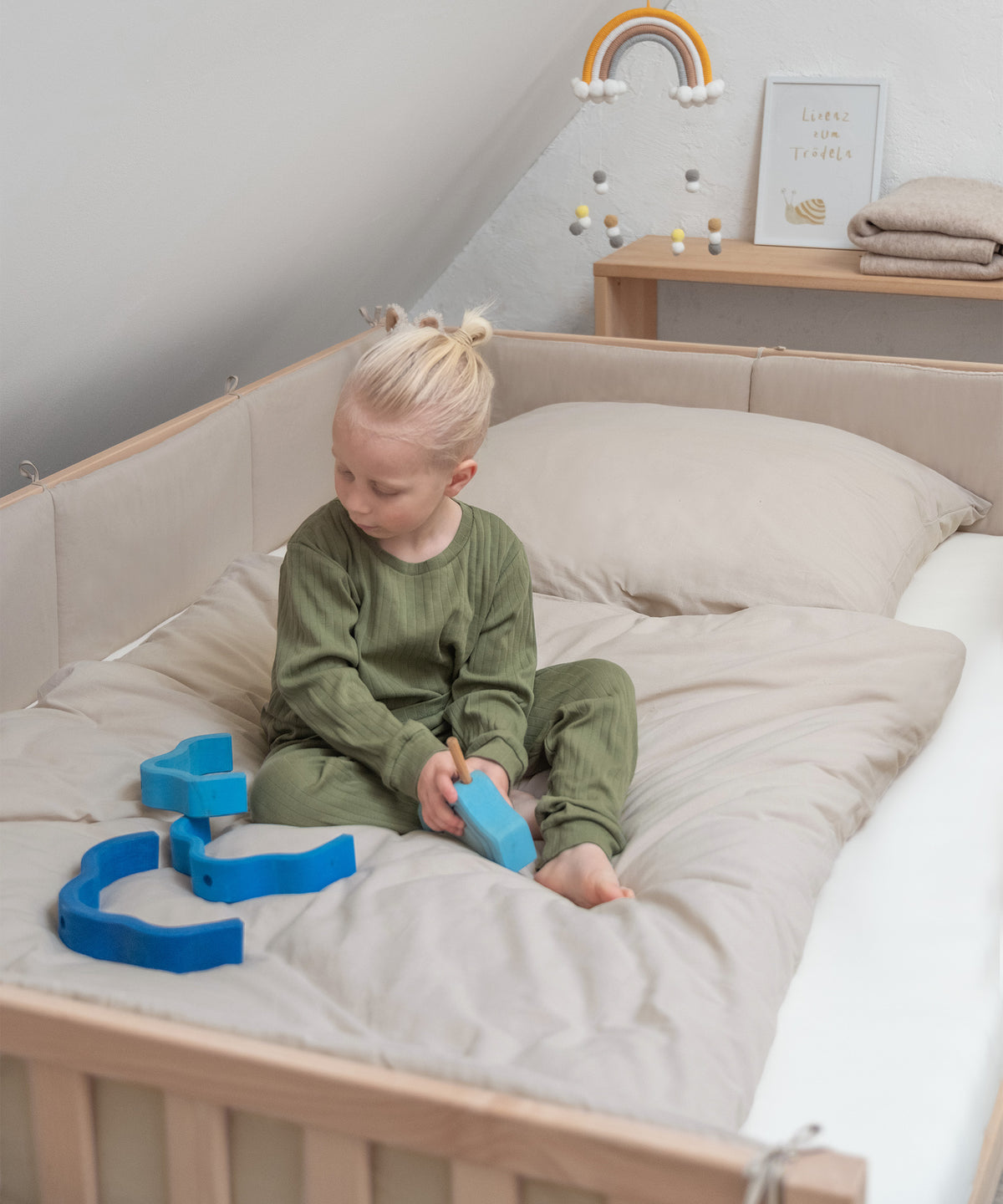 Kind sitzt auf Bett der Grlße 200 mal 120 cm mit Bettumrandung in Beige und spielt.