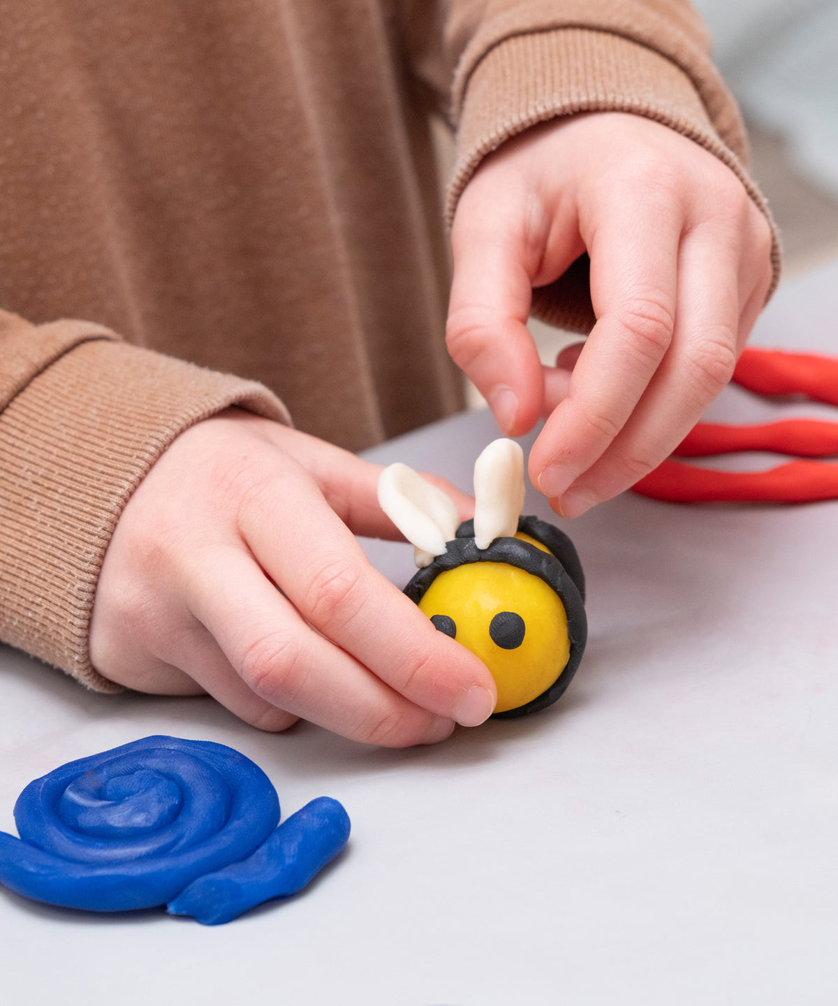 Kinderhände, die eine Biene aus Knete formen.