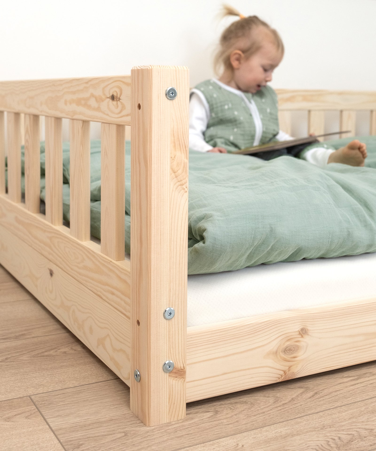 Nachhaltiges Kiefernholz*Unser Bodenbett wird aus nachhaltigem Kiefernholz unter fairen Arbeitsbedingungen gefertigt.|Nahaufnahme Kiefernholz, Mädchen sitzt im Bett und schaut ein Buch an.