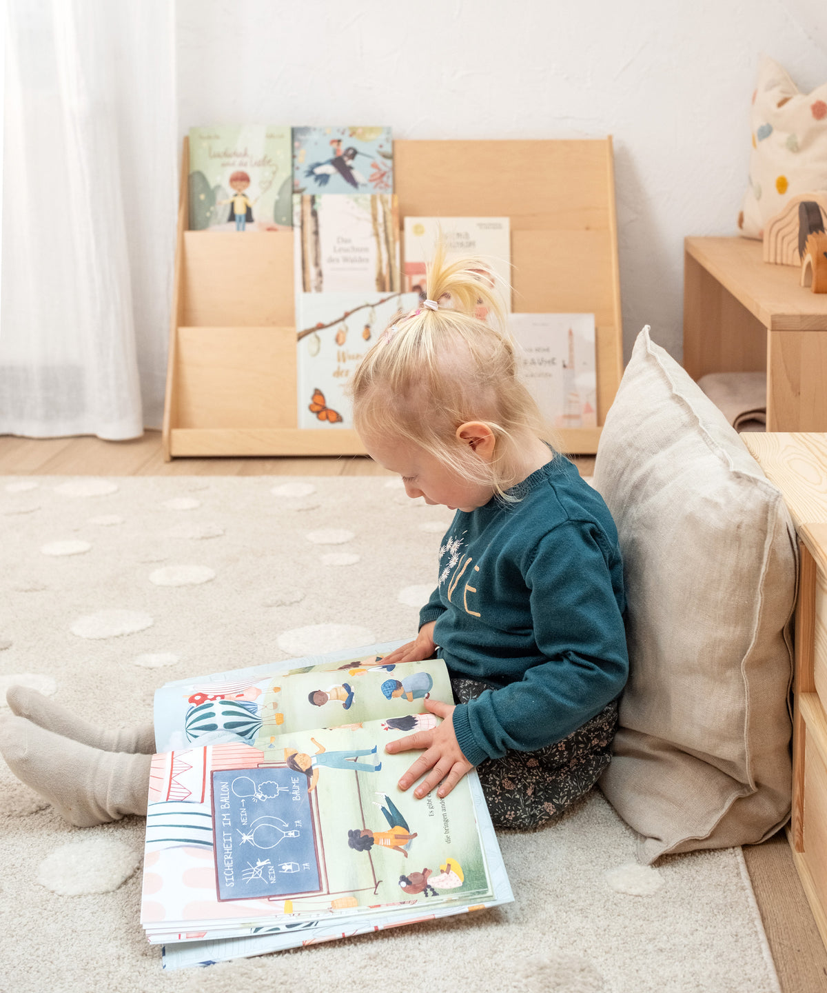 Ein Kind sitzt auf dem Boden vor dem Bücherregal und blättert konzentriert in einem Kinderbuch, während im Hintergrund das Regal mit weiteren Büchern bestückt ist.