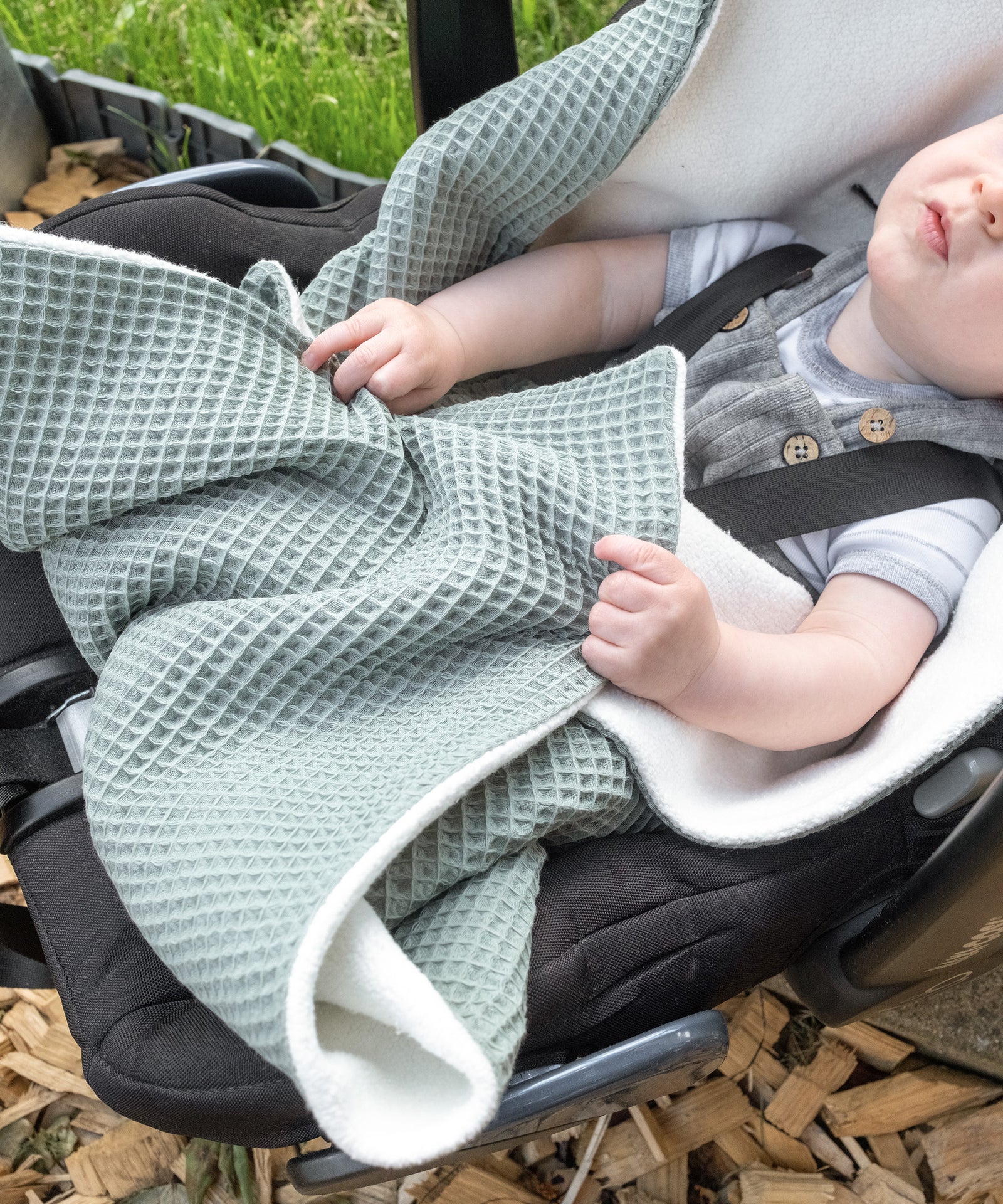 Baby mit Einschlagdecke in Babyschale.