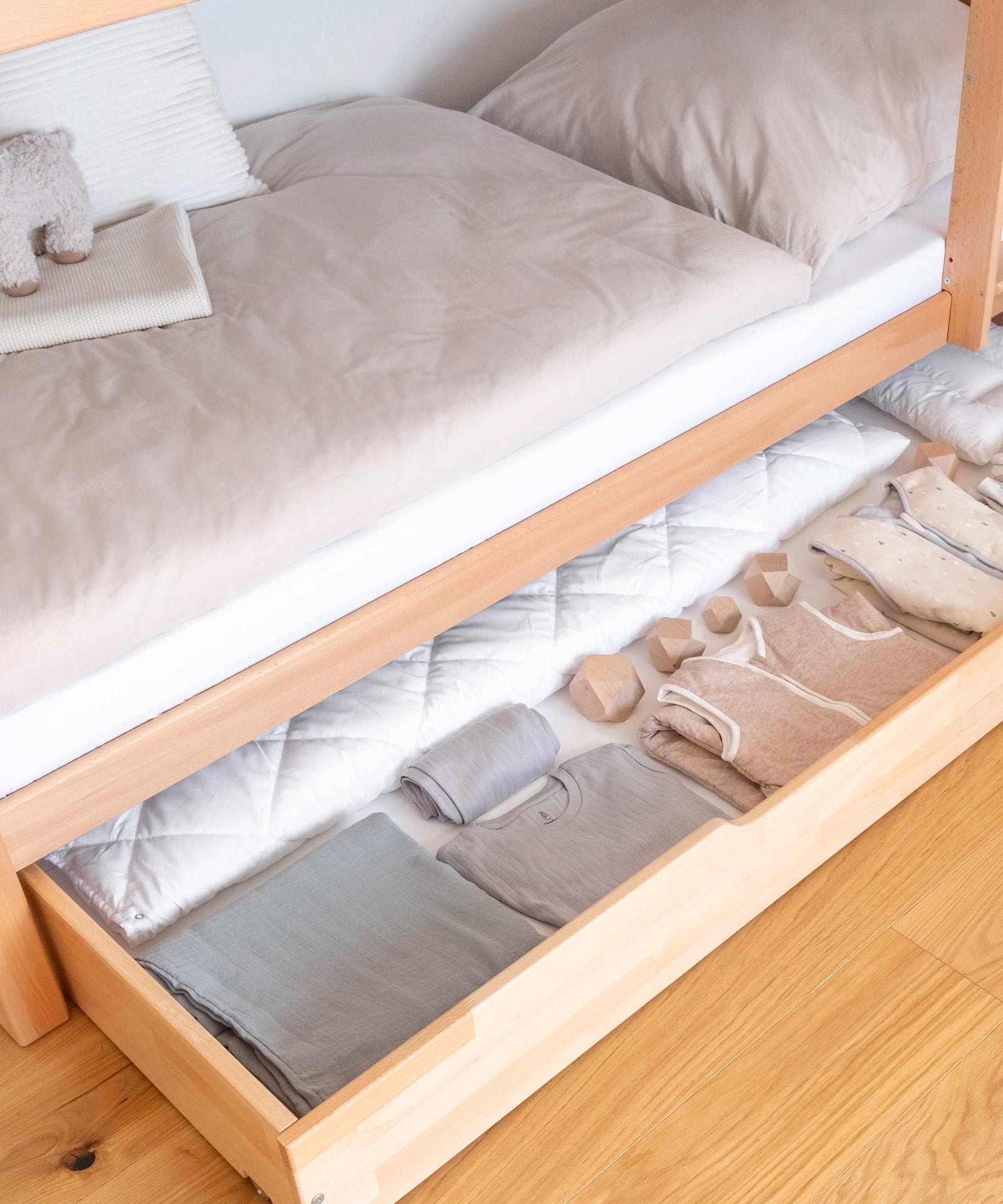 Zusätzlicher Stauraum*Unsere optionale Bettschublade bietet zusätzlichen Stauraum für Groß und Klein.|Detailansicht der befüllten Bettschublade in Natur.