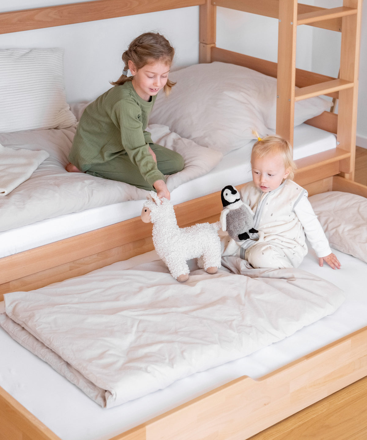 Mädchen sitzt im unteren Bett des Etagenbetts, auf dem ausgezogenen Bettkasten davor sitzt ein Geschwisterkind.