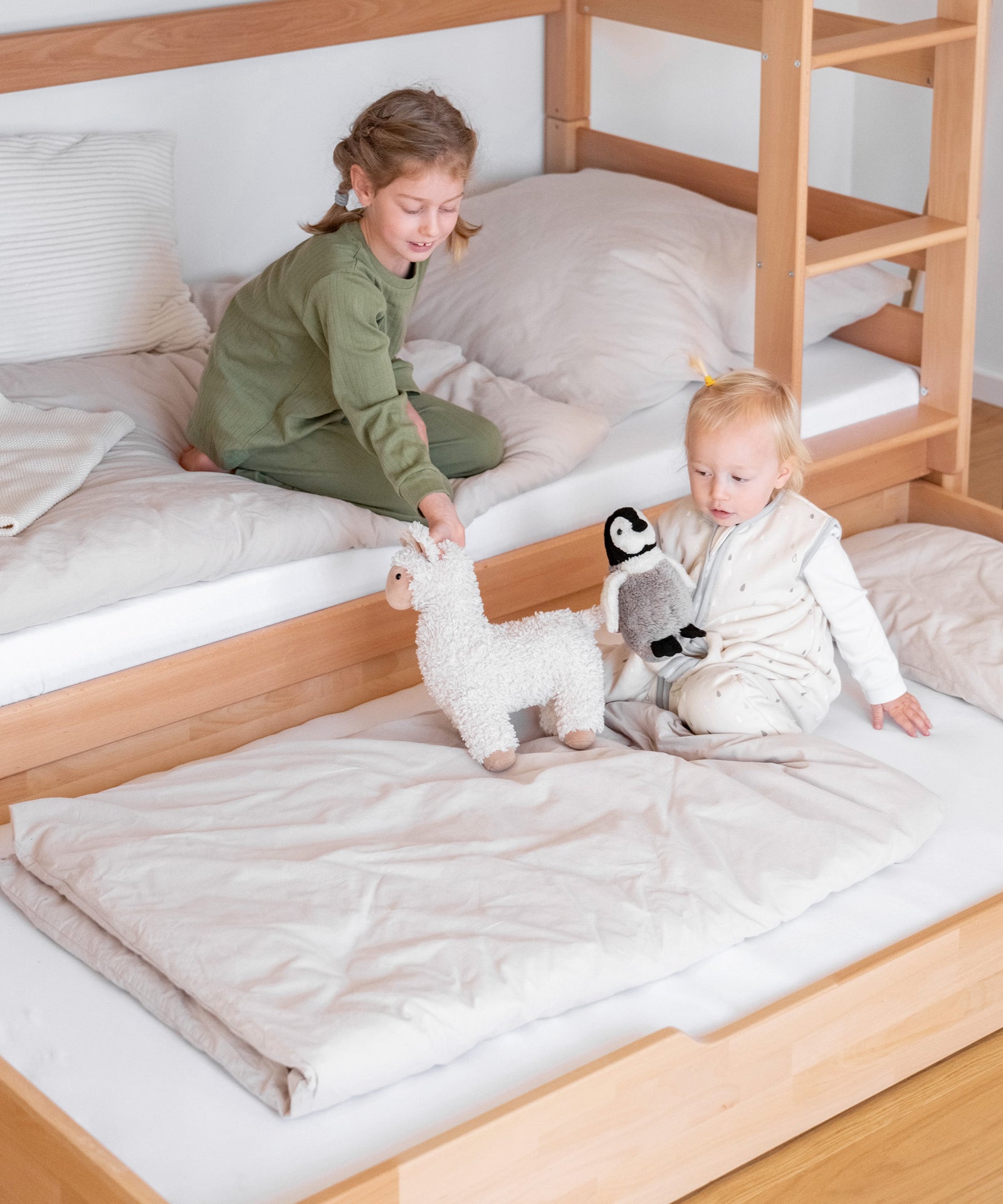 Zusätzlicher Schlafplatz*Für Übernachtungsgäste oder Eltern: Mit dem optionalen Bettkasten kann man ganz einfach einen weiteren Schlafplatz zaubern.|Mädchen sitzt im unteren Bett des Etagenbetts, auf dem ausgezogenen Bettkasten davor sitzt ein Geschwisterkind.