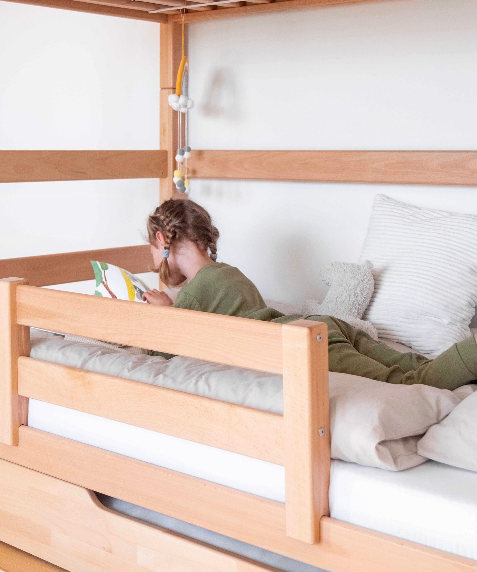 Mädchen liegt in Etagenbett und schaut ein Buch an.