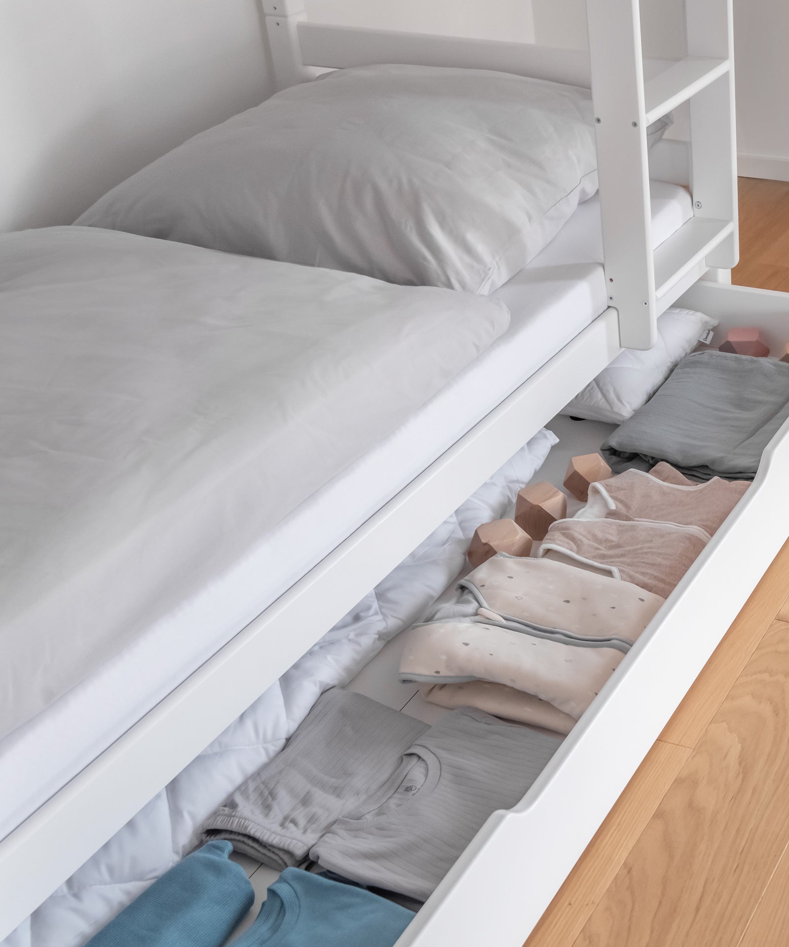 Zusätzlicher Stauraum*Unsere optionale Bettschublade bietet zusätzlichen Stauraum für Groß und Klein.|Detailansicht der befüllten Bettschublade in Weiß.