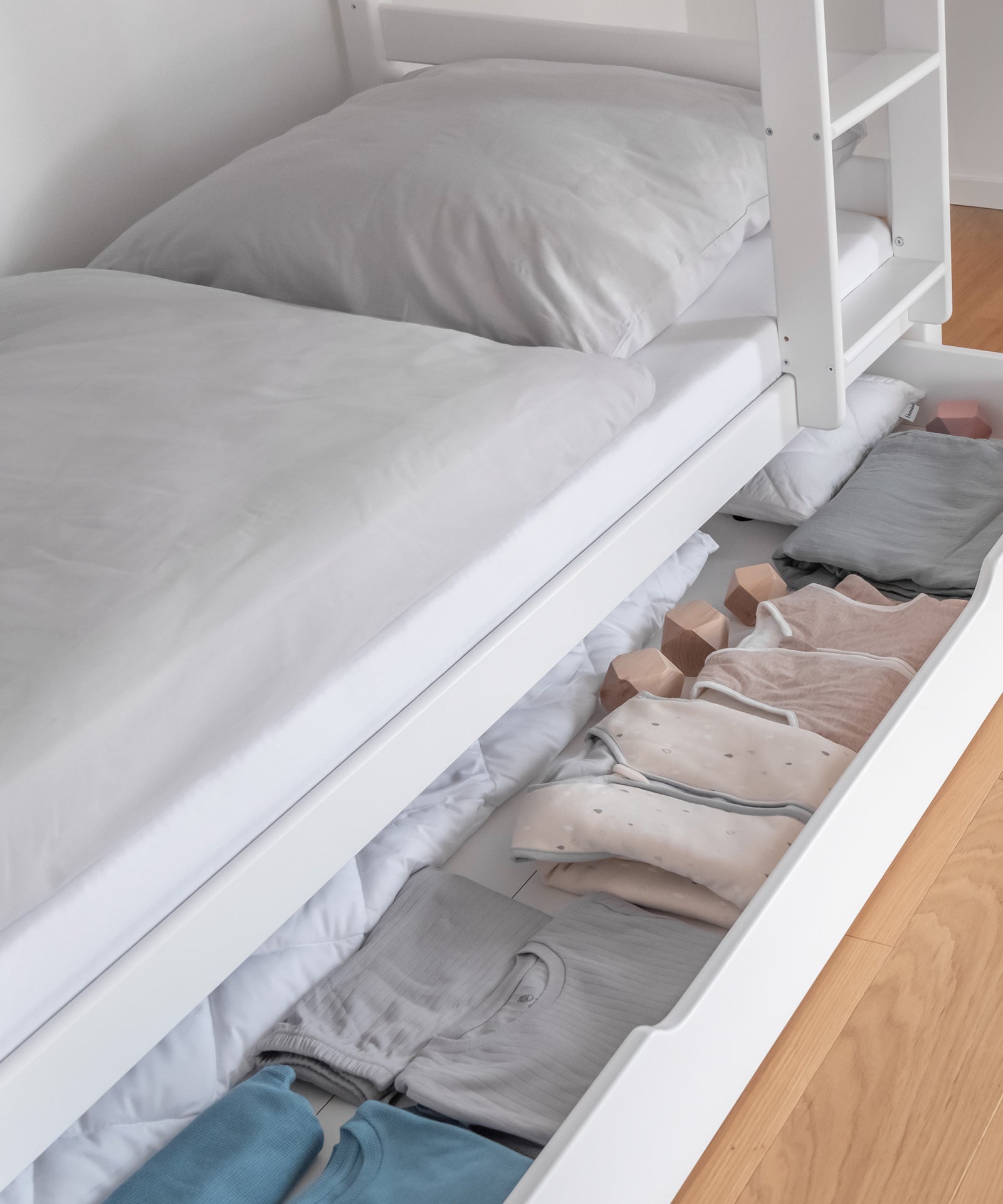 Zusätzlicher Stauraum*Unsere optionale Bettschublade bietet zusätzlichen Stauraum für Groß und Klein.|Detailansicht der befüllten Bettschublade in Weiß.