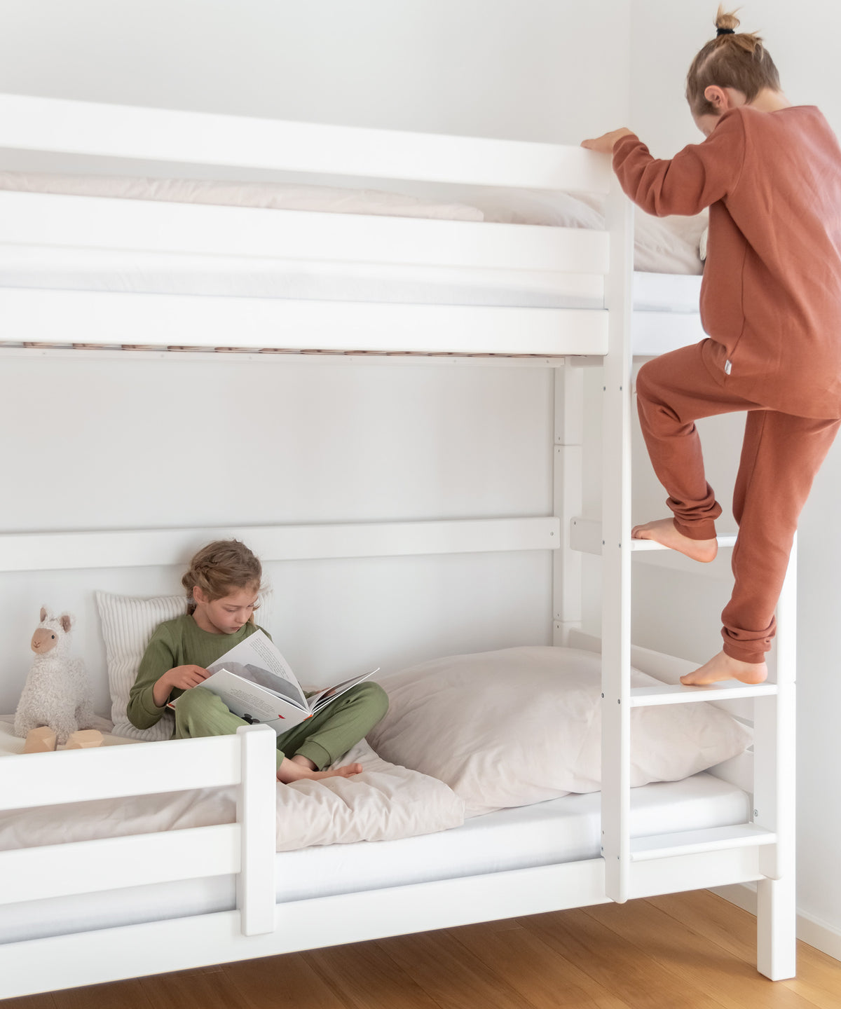 Zwei Geschwisterkinder sind auf dem Etagenbett, ein Mädchen schaut unten ein Buch an, ein Junge steigt die Leiter nach oben.