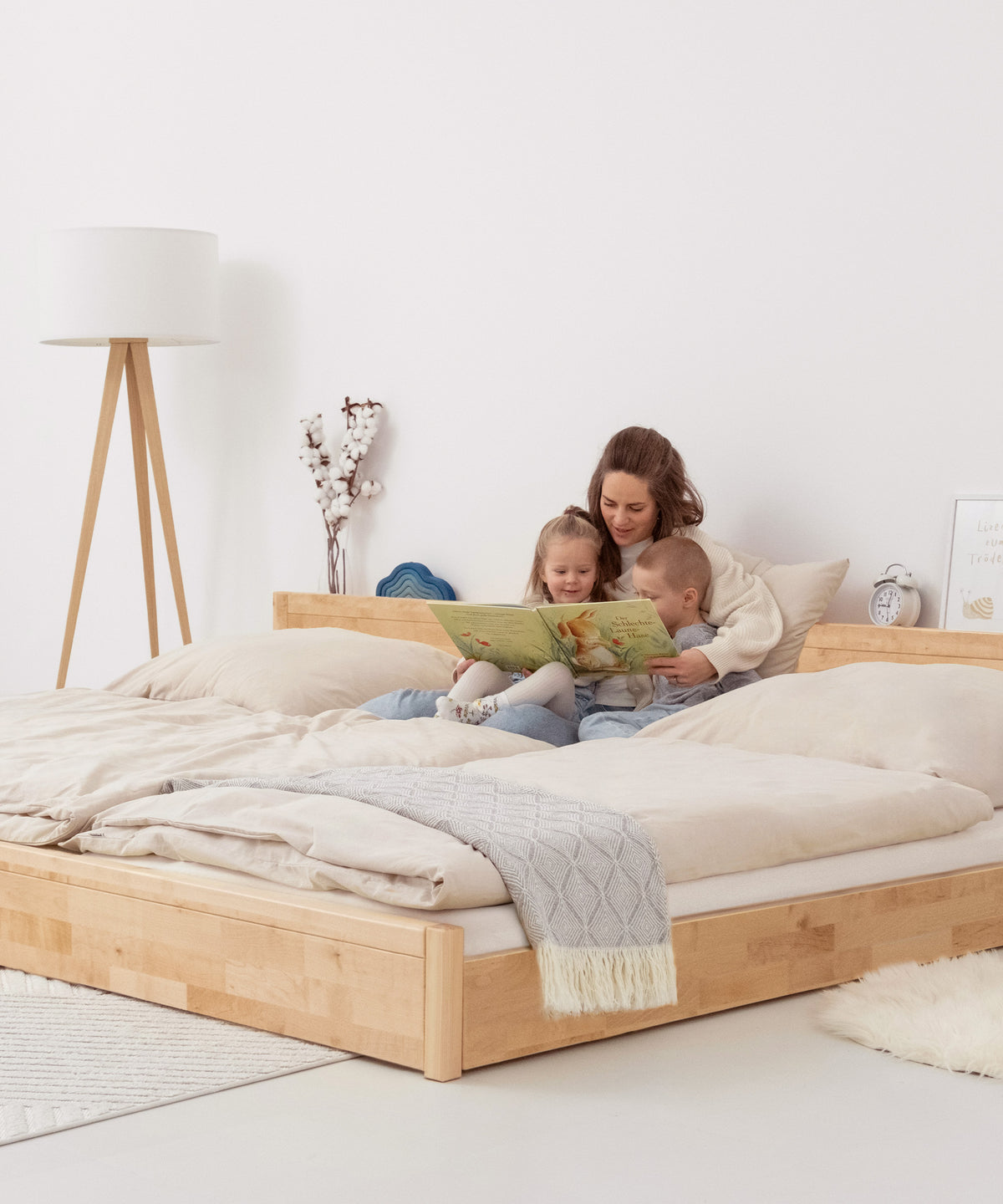 Mutter mit Kindern schaut Bilderbuch an auf Familienbett Birke bodentief.