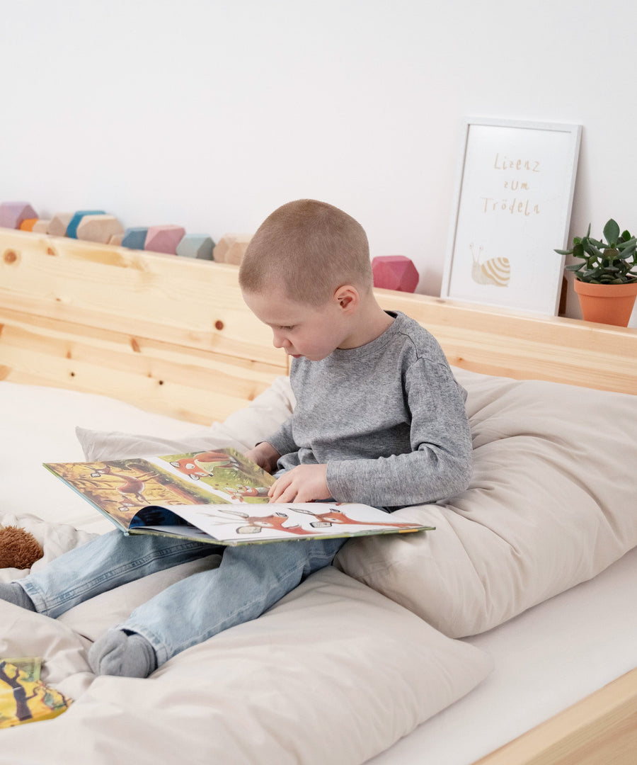 Junge sitzt in Familienbett Kiefer und schaut ein Buch an.