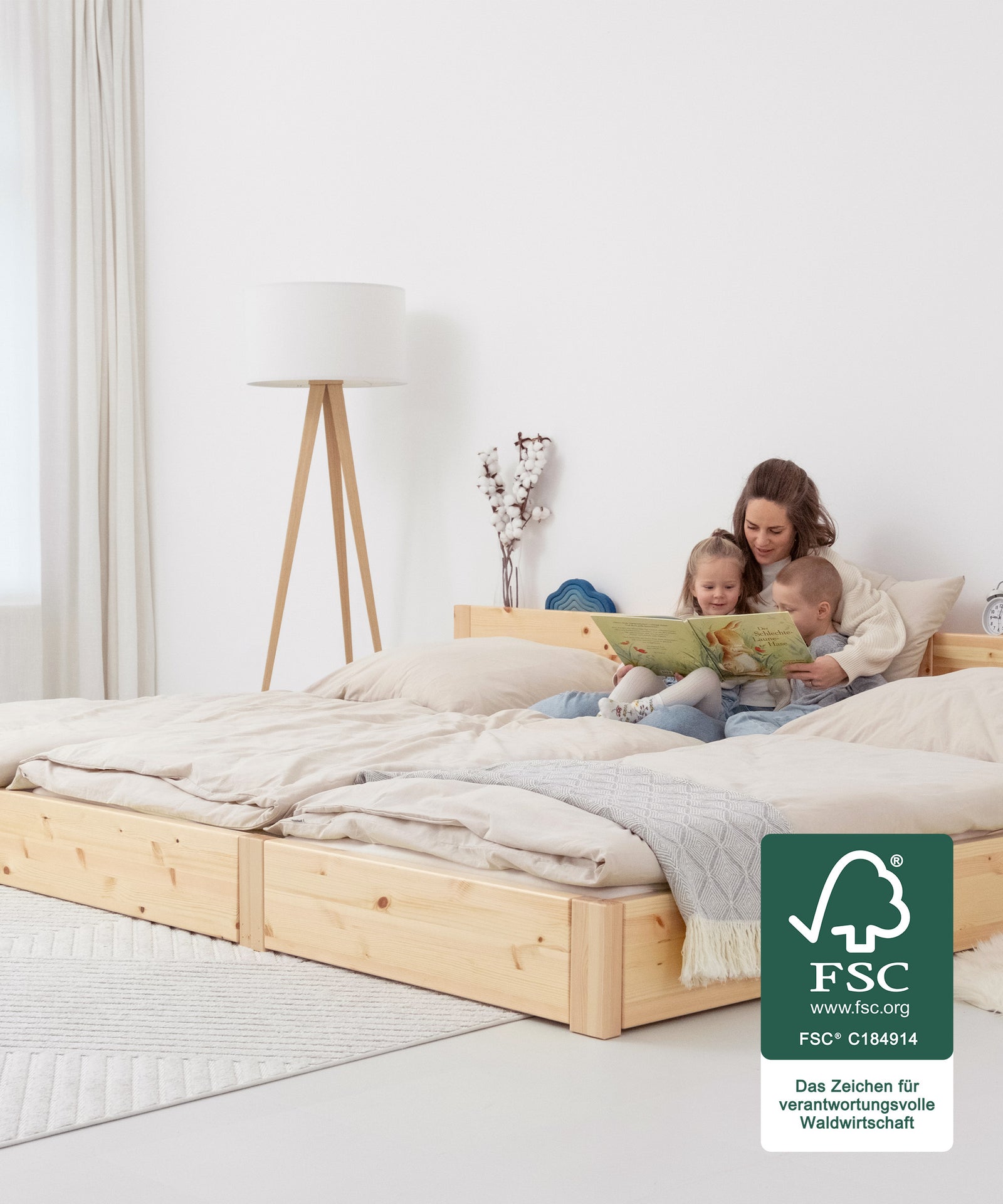 Platz für die ganze Familie**Das Familienbett bietet eine durchgehende, großzügige Liegefläche. So wird Co-Sleeping komfortabel und erholsam.|Familie sitzt auf Familienbett natur bodentief und schaut ein Buch an.