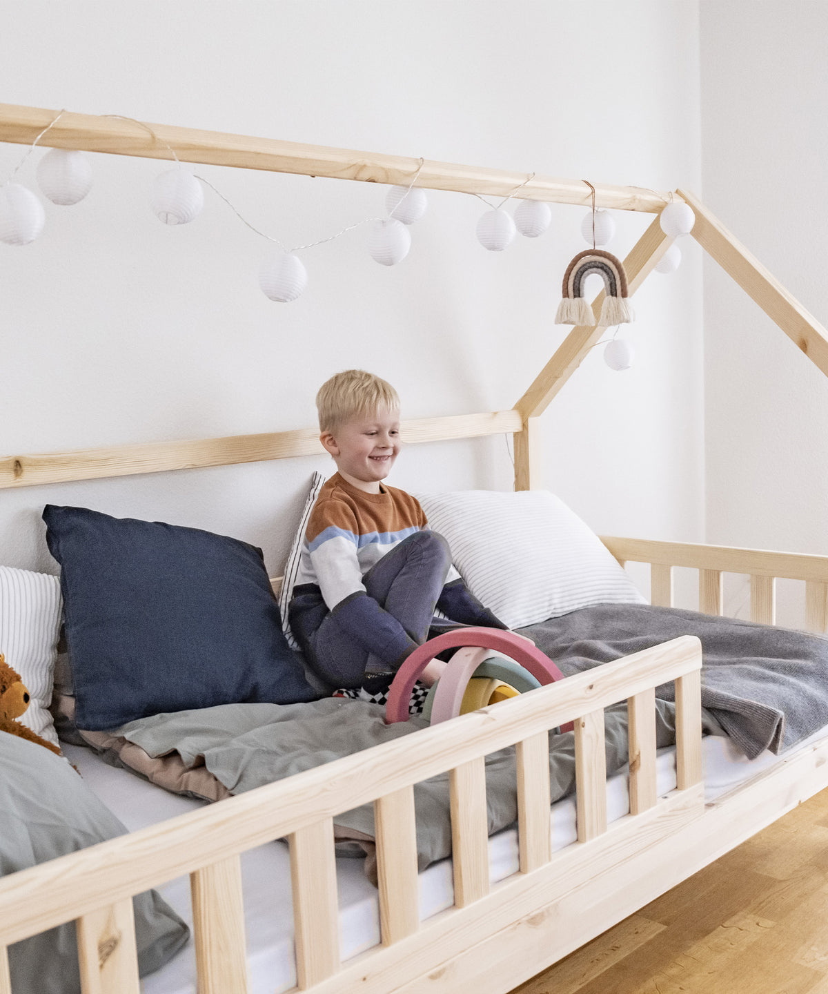Hausbett mit Rausfallschutz für Kinder, Junge sitzt im Bett und spielt.