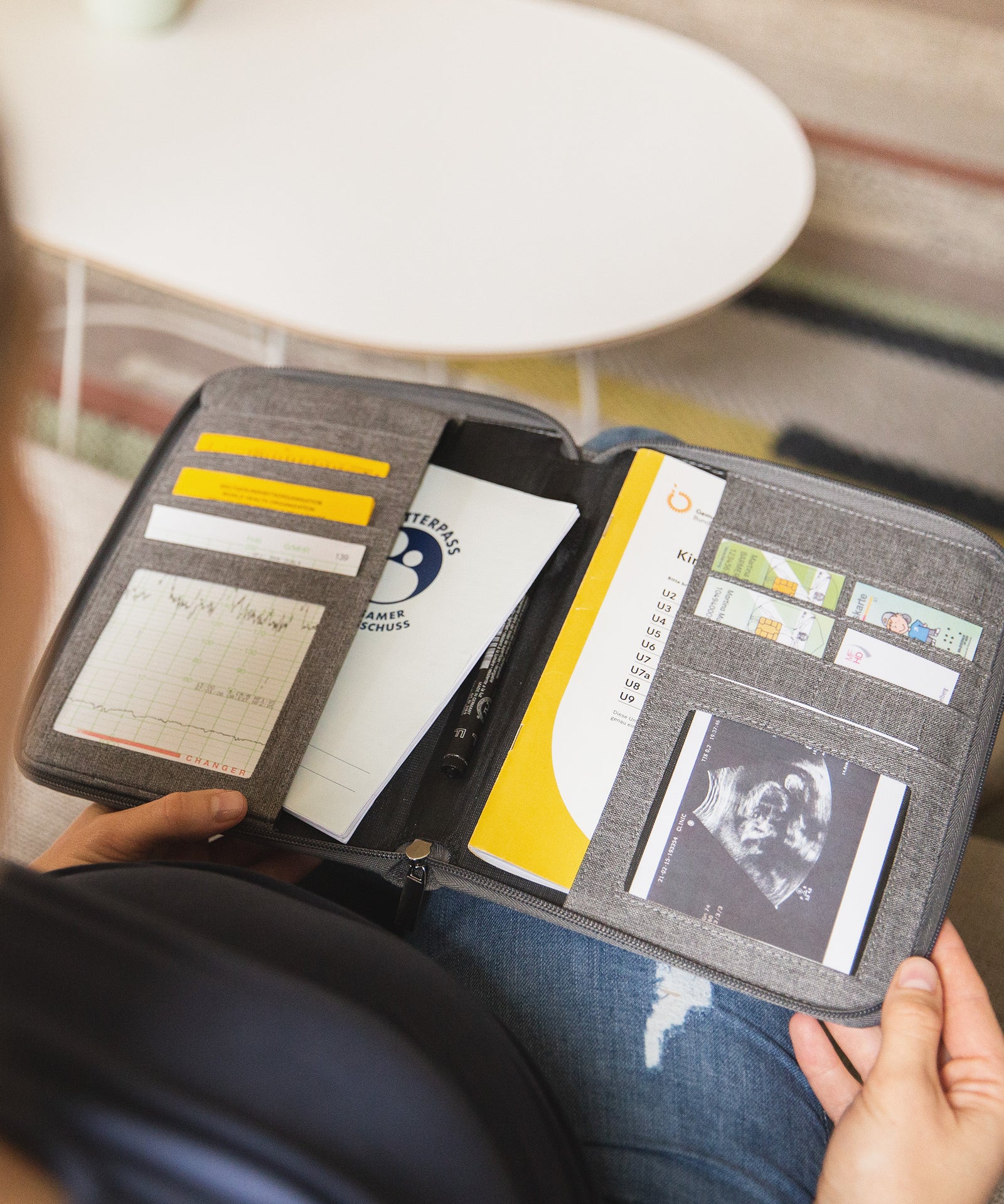 Viel Platz*Keine losen Kärtchen und Hefte mehr! Hier passt alles rein: Impfpass, Mutterpass, U-Heft, Versichertenkarte, Ultraschallbilder.|Schwangere Frau blickt in ihre Mutterpasshülle. Darin befinden sich Impfpass, Mutterpass, U-Heft, Versichertenkarte, Ultraschallbilder und weiteres.