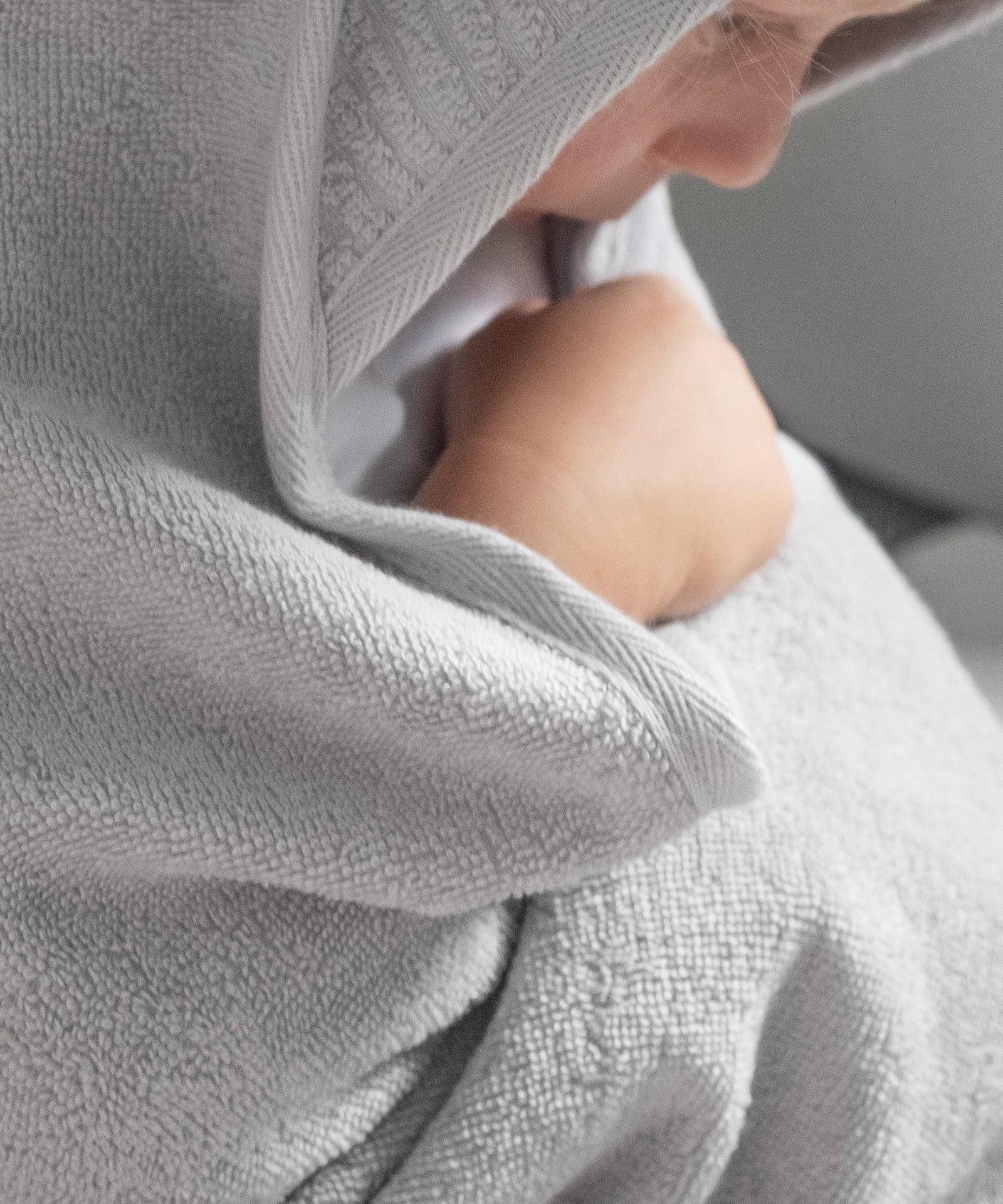 Perfekt zum Einkuscheln*In der Größe 100 × 100 cm ist das Kapuzenhandtuch besonders komfortabel, ob nach dem Baden zuhause oder unterwegs.|Kind kuschelt sich in Kapuzenhandtuch Hellgrau ein.