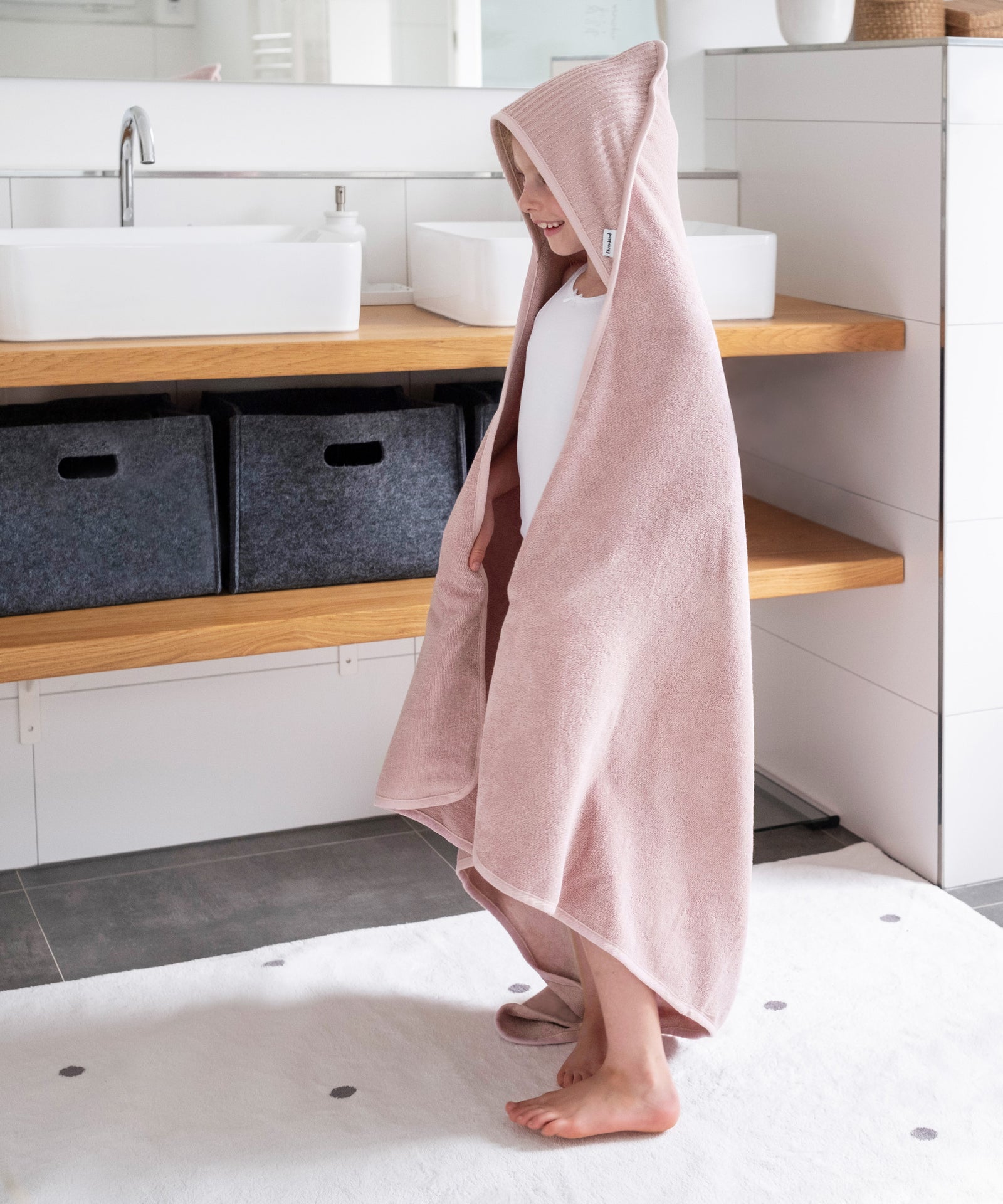 Mädchen mit Kapuzenhandtuch in Rosé steht in Badezimmer.