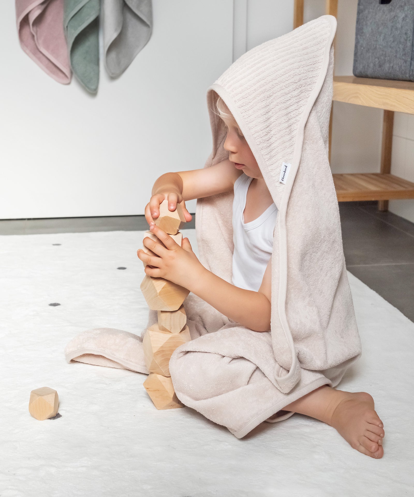 Kind mit Kapuzenhandtuch Beige spielt mit Balanciersteinen.