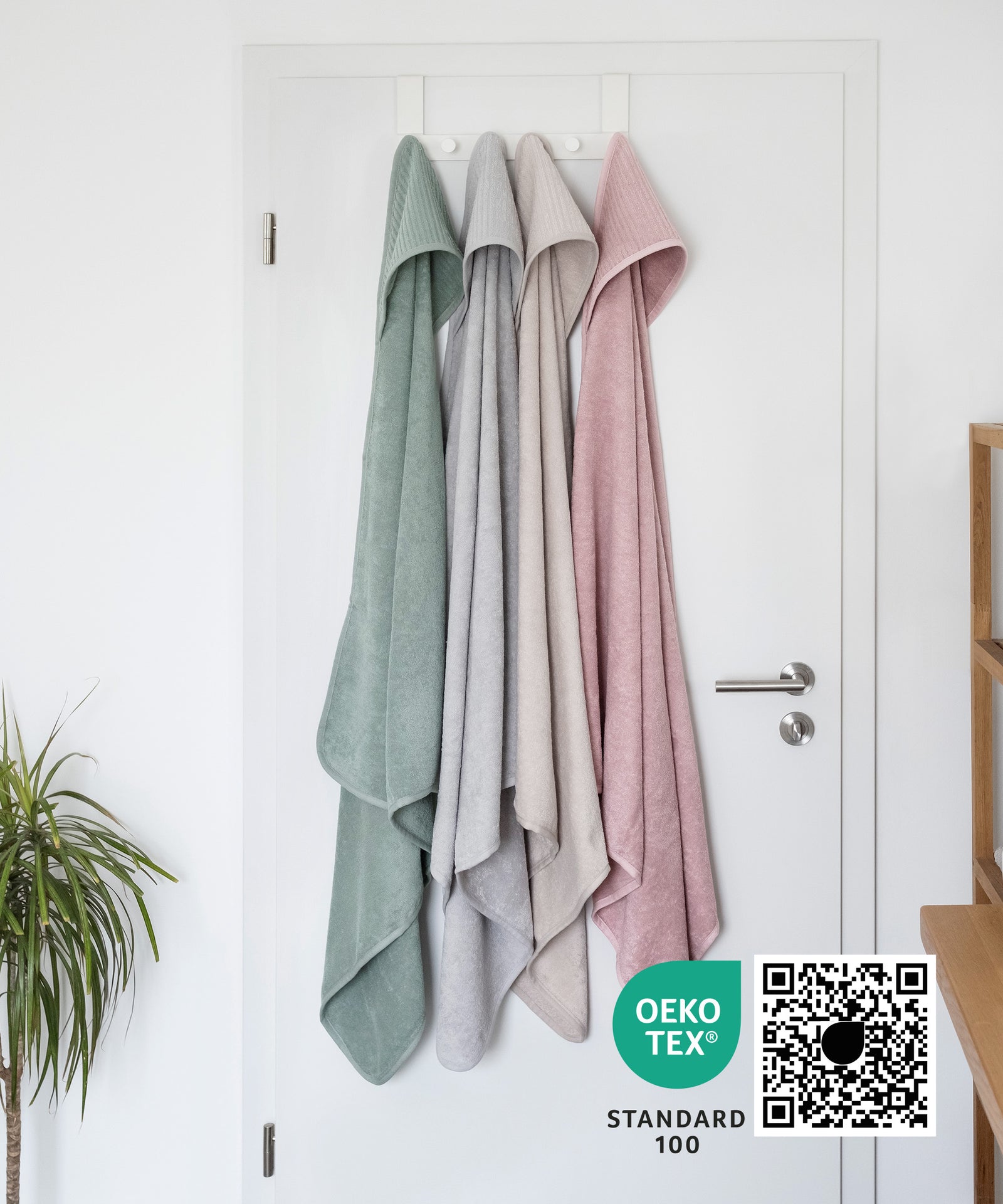 Kapuzenhandtuch in vier Farben hängt an Badezimmertüre, Kapuzenhandtuch ist Oeko-Tex zertifiziert.