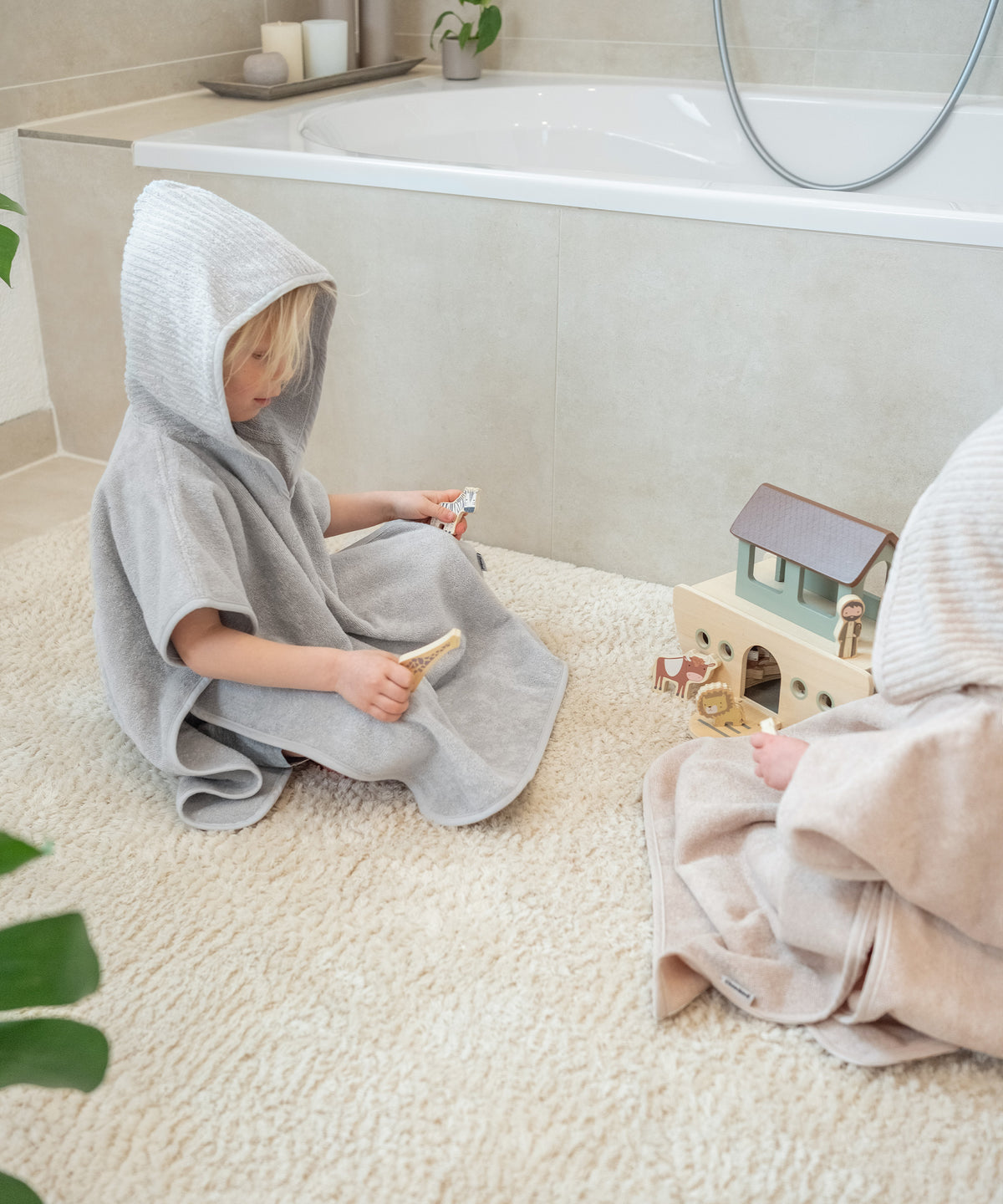 Kind in Badeponcho Hellgrau spielt auf Badezimmer-Teppich.