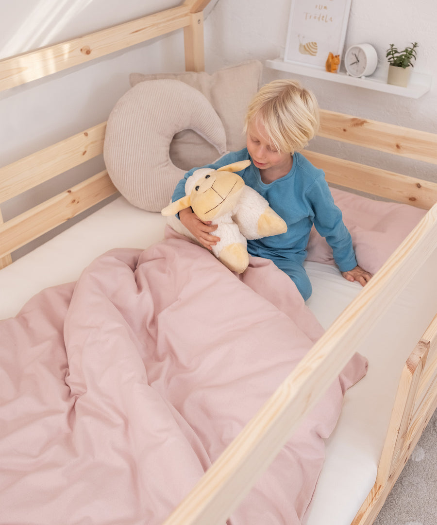 Kind sitzt in Bett mit Feinbiber Bettwäsche in Rosé.