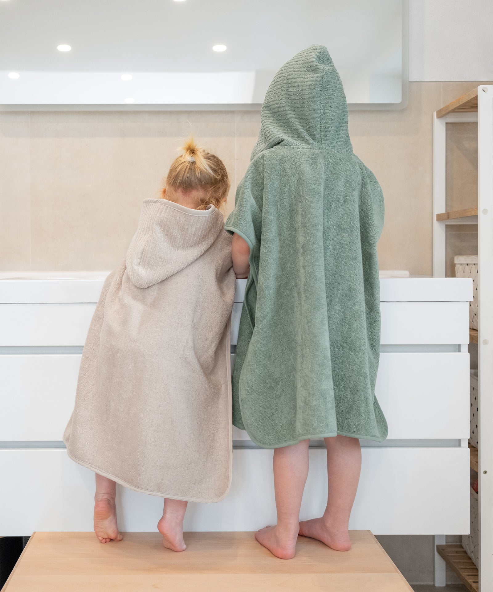 Eine Größe für alle*Der Badeponcho in Einheitsgröße eignet sich optimal für Kinder von ca. 1 bis 5 Jahren.|Zwei Kinder stehen auf Hocker an Waschbecken im Bad.