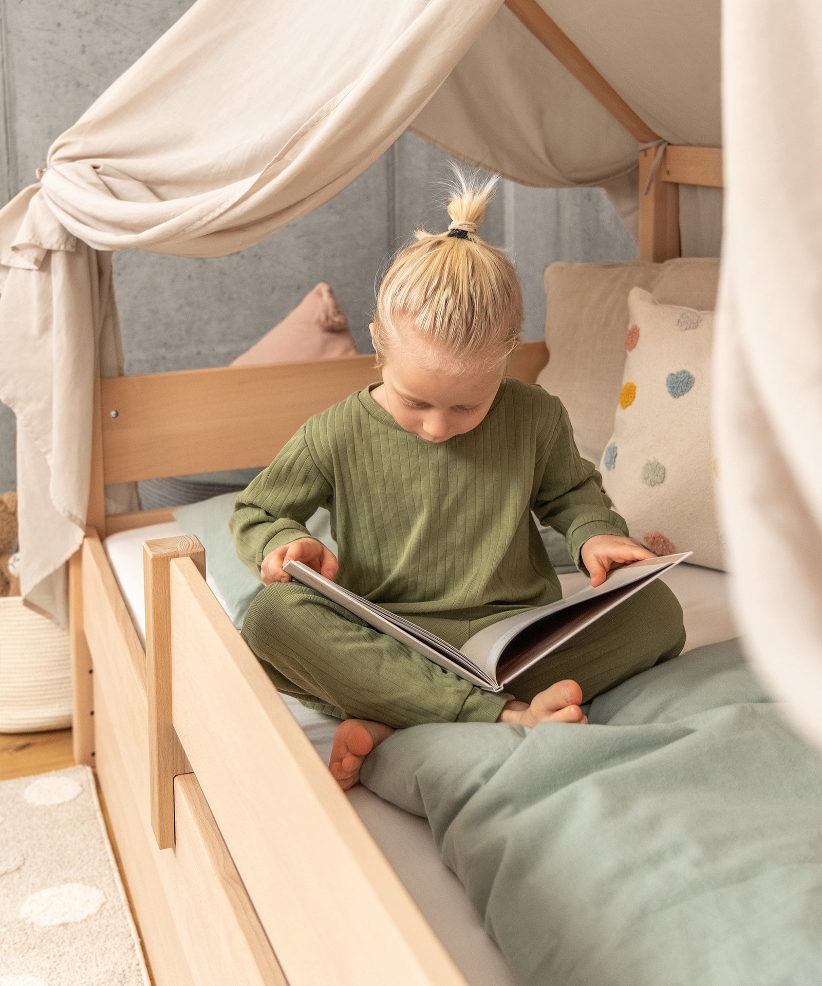 Kind sitzt im Hausbett und liest ein Buch.