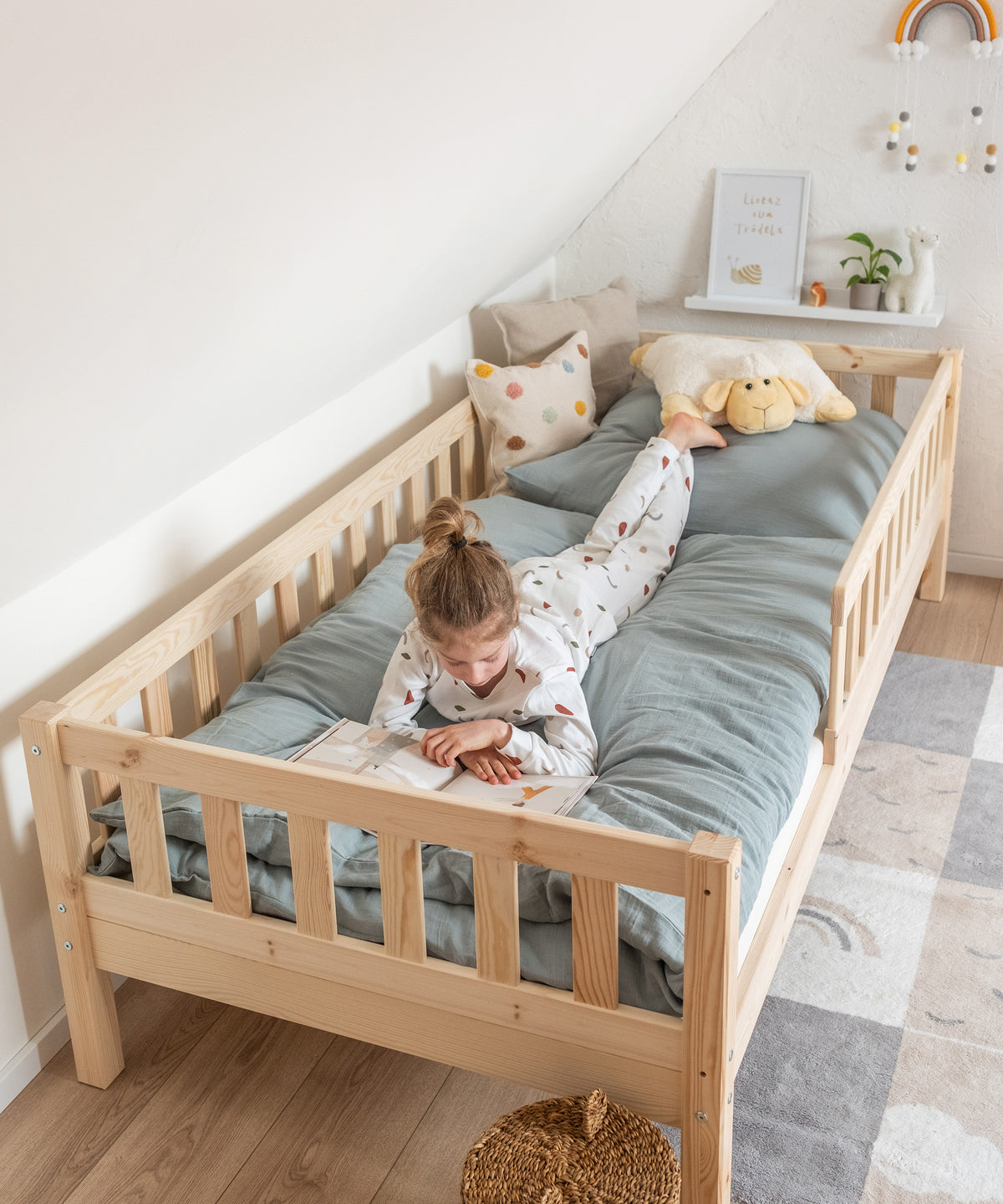 Mädchen liegt in Kinderbett Kiefer Natur und schaut ein Buch an.