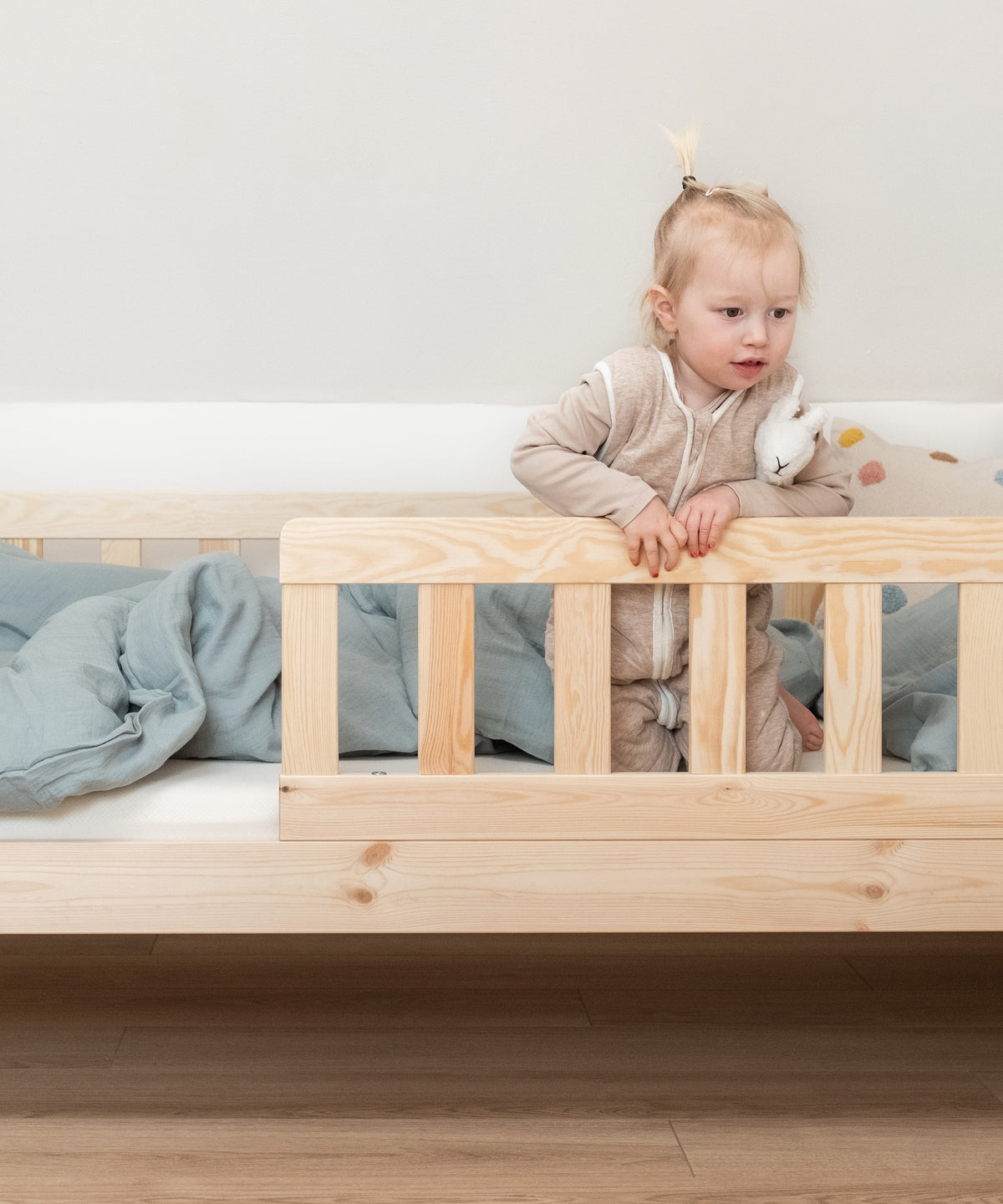 Kind sitzt in Kinderbett Kiefer Natur und schaut über den praktischen Rausfallschutz.