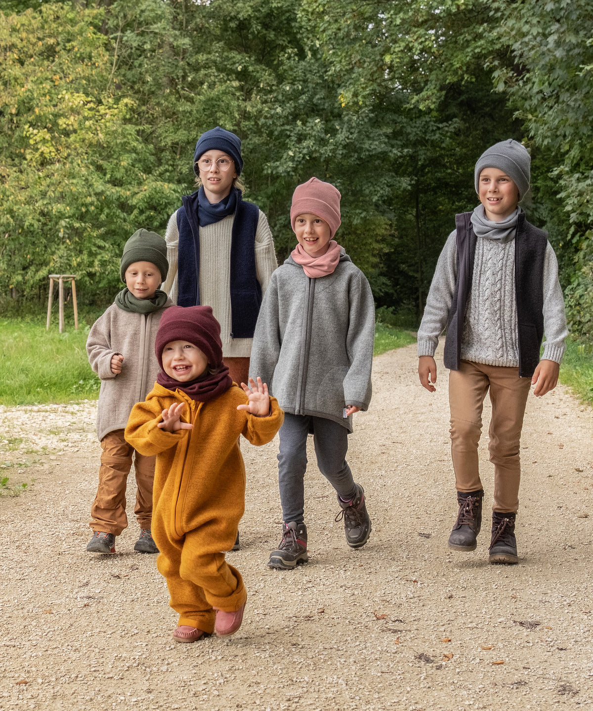 Fünf Kinder von klein bis groß laufen auf einem Waldweg.