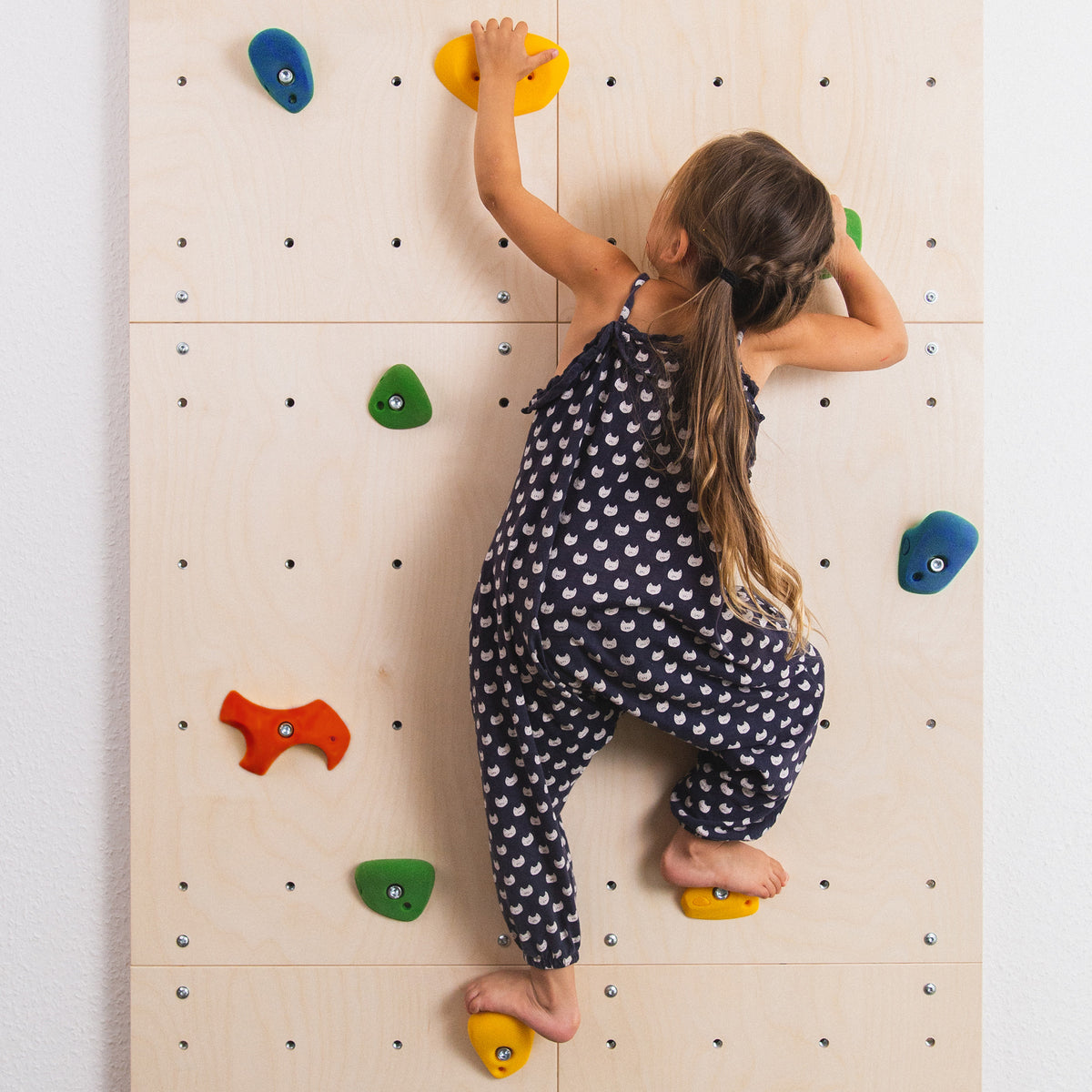 Mädchen klettert an Kletterwand mit montierten Klettergriffen.