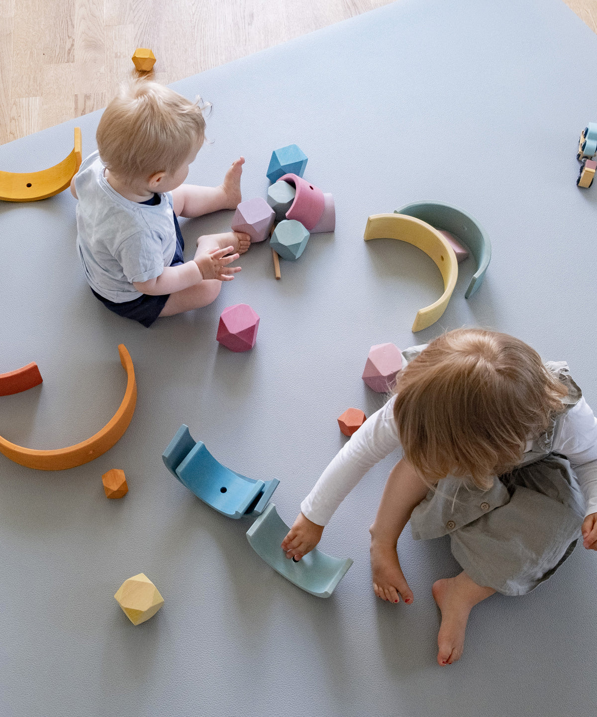 Zwei Kinder spielen mit Holzspielzeug auf Krabbelmatte PRO hellgrau.