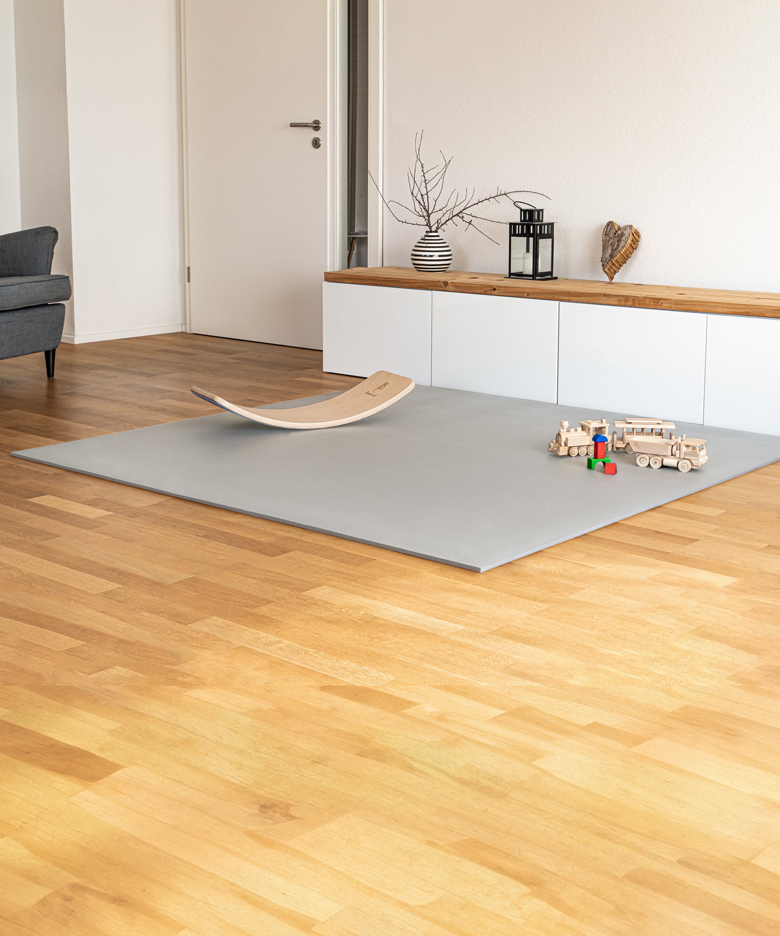 Schützt vor kalten Füßen*Die Krabbelmatte PRO ist stoßdämpfend, wärmeisolierend und auch für Böden mit Fußbodenheizung geeignet.|Krabbelmatte PRO mit Rutschbrett liegt in Wohnzimmer.