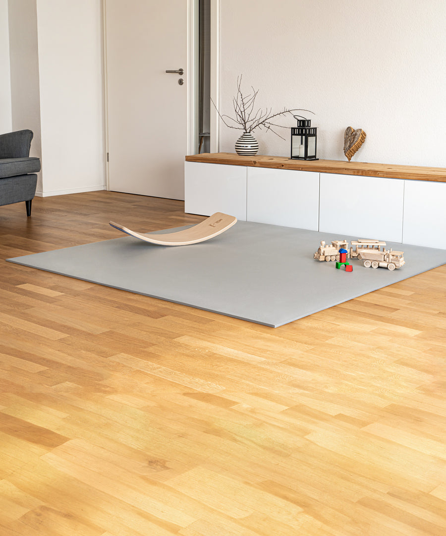 Schützt vor kalten Füßen*Die Krabbelmatte PRO ist stoßdämpfend, wärmeisolierend und auch für Böden mit Fußbodenheizung geeignet.|Krabbelmatte PRO mit Rutschbrett liegt in Wohnzimmer.