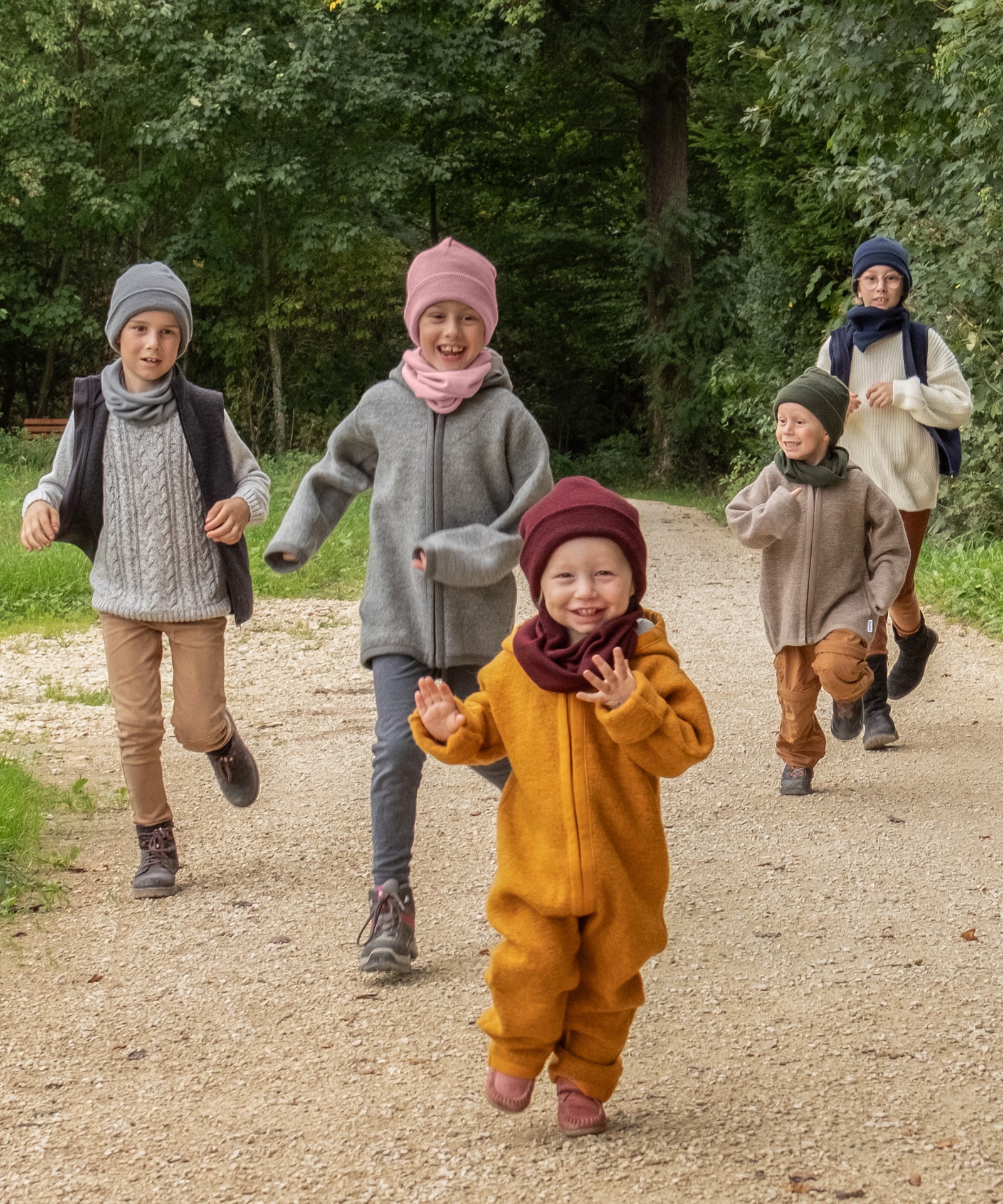 Eine Größe für alle*Der Schlauchschal lässt sich einfach und bequem über den Kopf ziehen. So passt der Schal allen Kindern von ca. 2 bis 12 Jahren.|Fünf Kinder von klein bis groß laufen auf einem Waldweg.