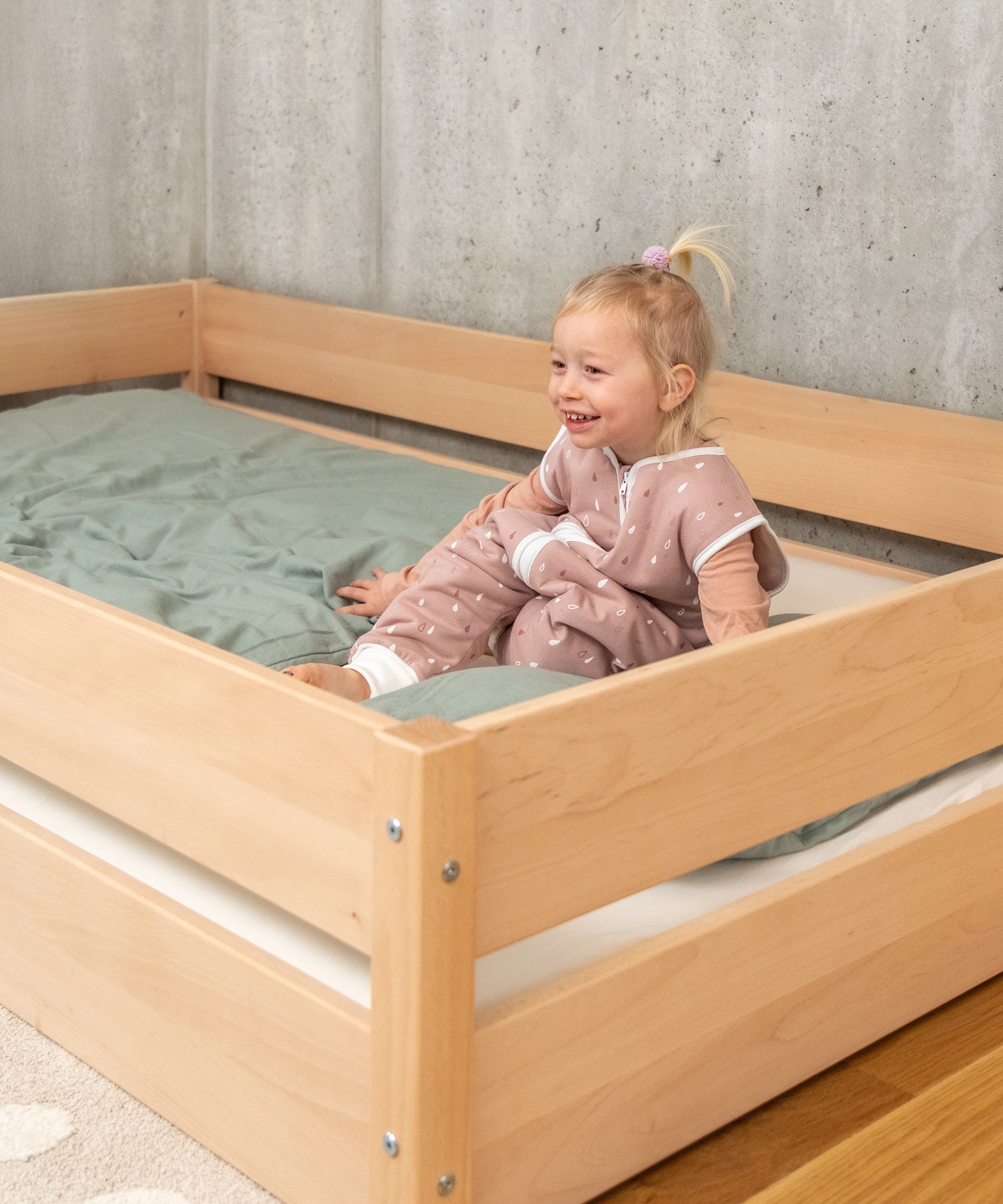 Mädchen sitzt in Bodenbett, Bodenbett ist Kinderbett nach dem Montessori Prinzip.