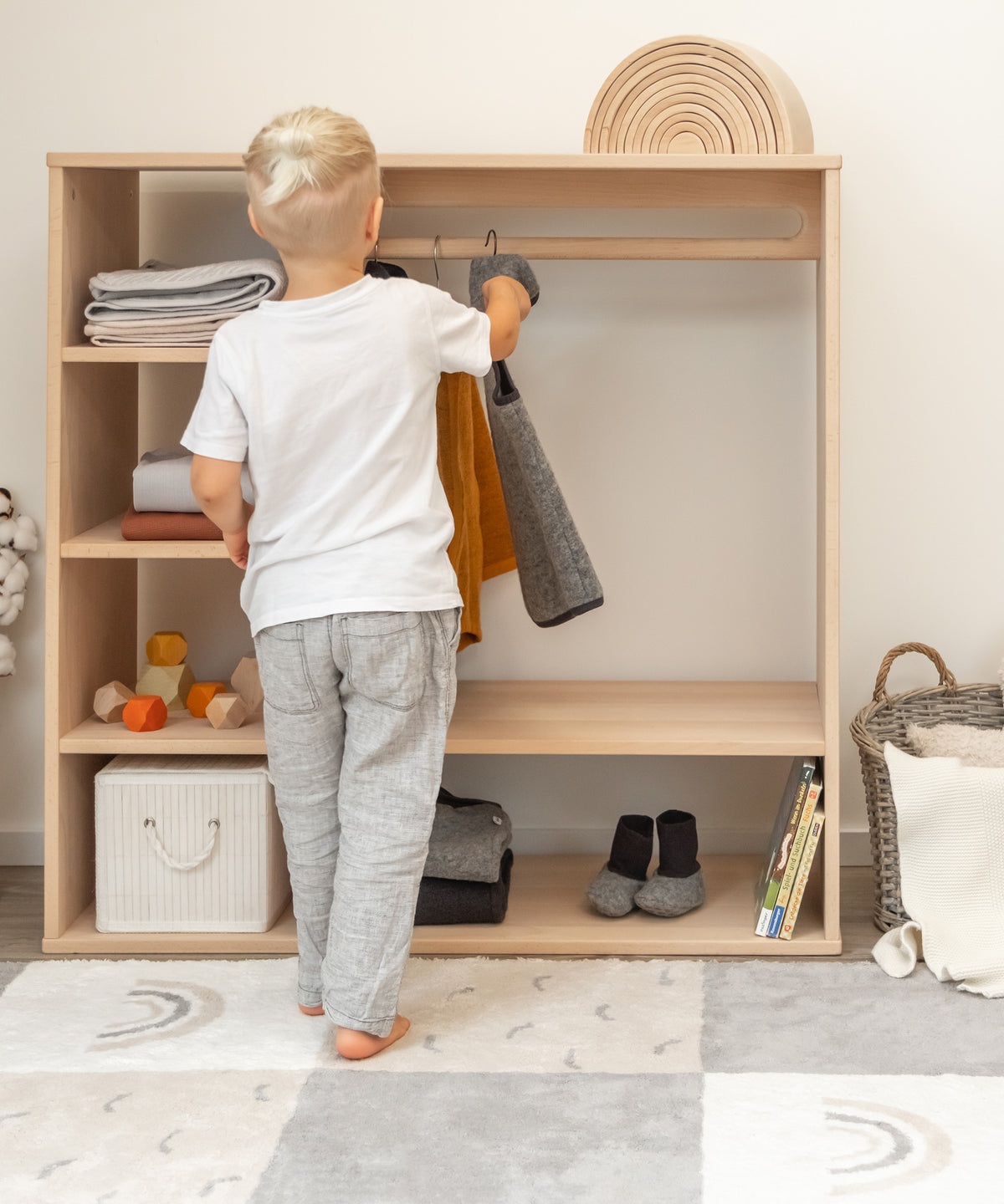 Junge hängt Walkweste in den Montessori Kleiderschrank.