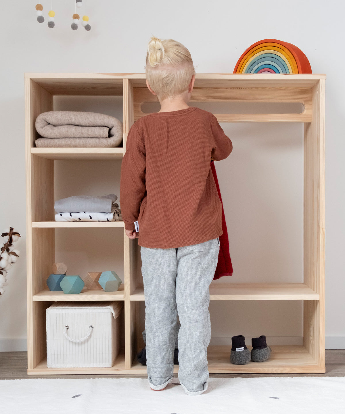 Kind hängt Kleidungsstück alleine in Montessori Kleiderschrank.