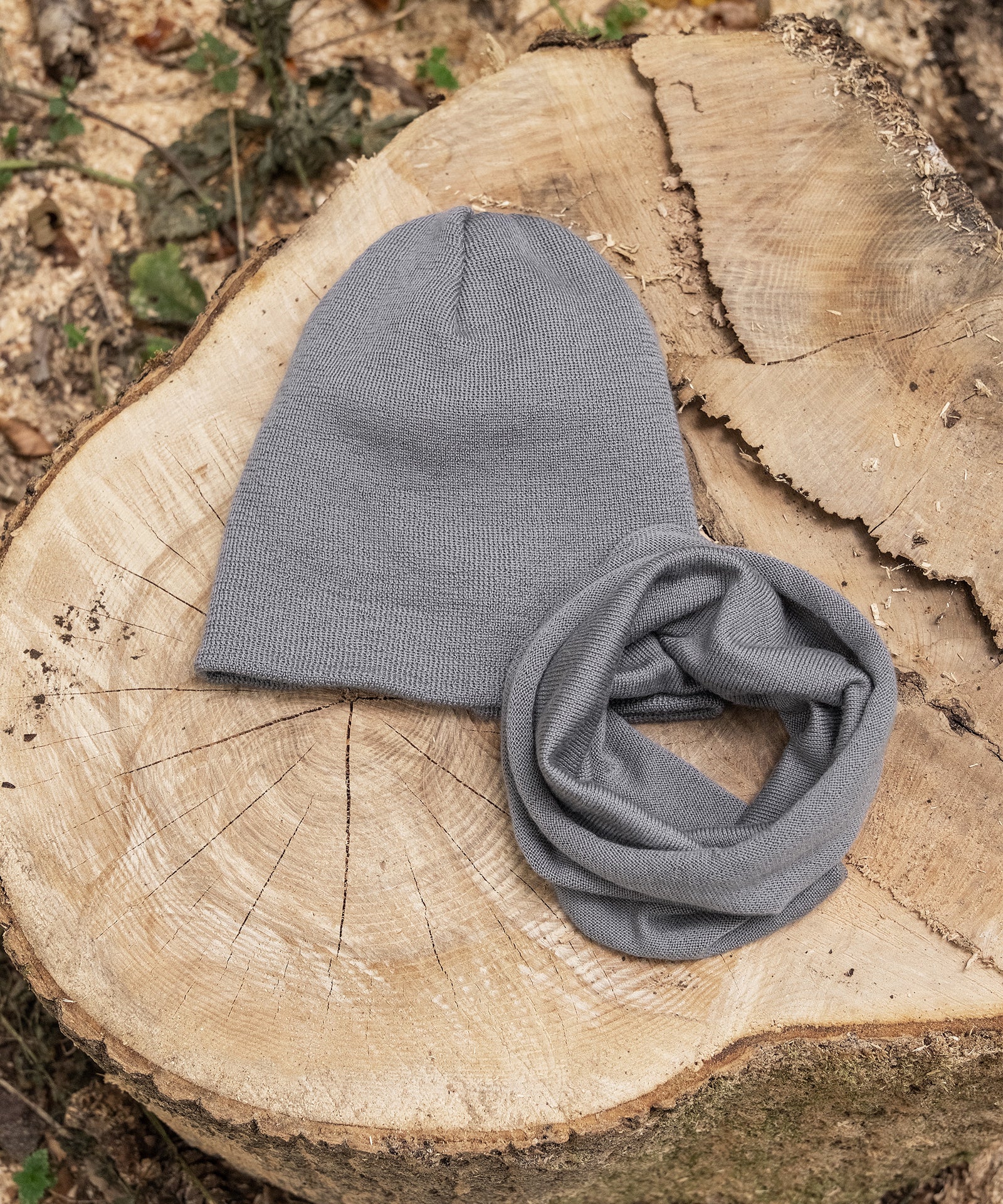 Passend erhältlich*Passend zur Strickmütze ist der Schlauchschal im Shop erhältlich.|Strickmütze und Schlauchschal in Grau liegen auf Baumstumpf.