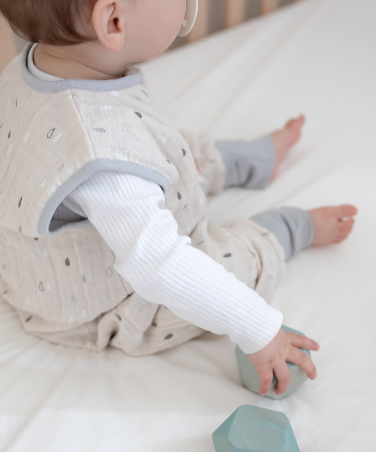 Baby mit Musselin Schlafsack mit Beinen sitzt in Bett.